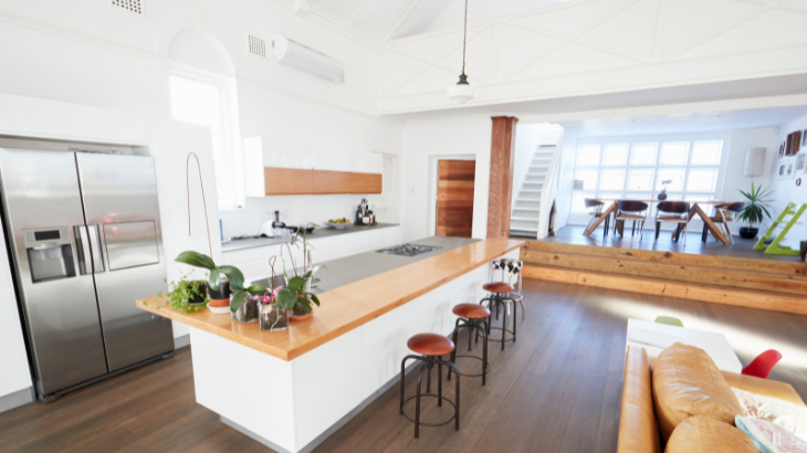 Modern kitchen with island, stainless steel fridge, and open living area with wooden floors.