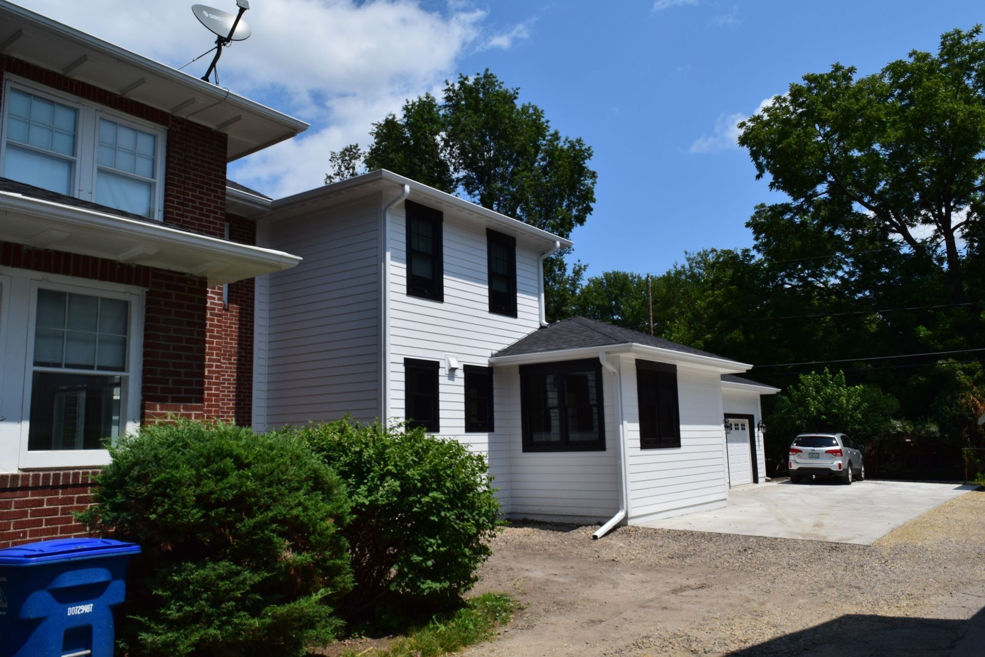 White two-story house with black window frames, small garage, and a brick house to the left. Car parked in driveway.
