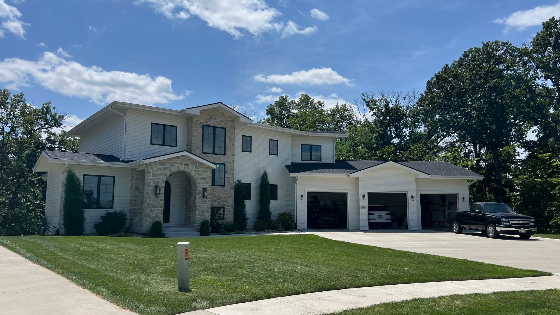 White two-story house with stone archway, black windows, and attached three-car garage; truck in driveway.