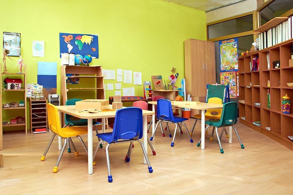 Classroom with child-sized tables and chairs, shelves with toys, and a world map on the wall.