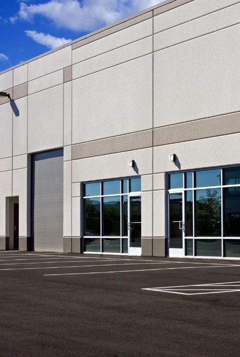 Industrial building exterior with loading door, windows, and asphalt parking area.
