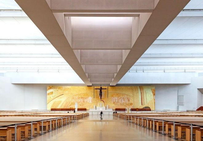 Interior view of a modern church with rows of pews and a large crucifix against a golden backdrop.