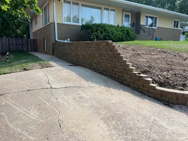 A house with a concrete driveway and a stone wall in front of it.