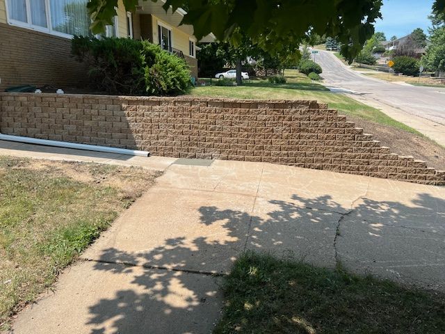 A brick wall is sitting next to a sidewalk in front of a house.