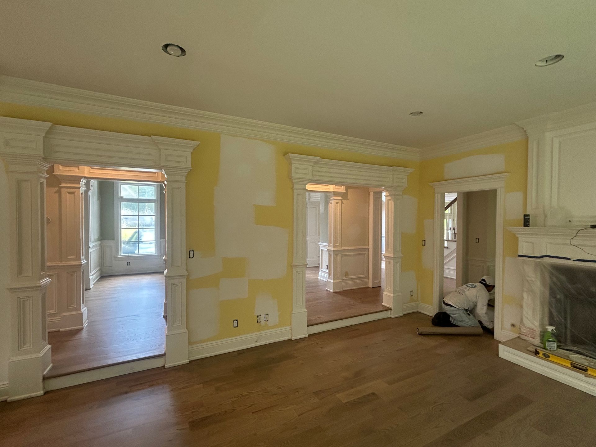 Interior room under renovation, with doorways, crown molding, fireplace, and hardwood flooring. Yellow paint on walls.