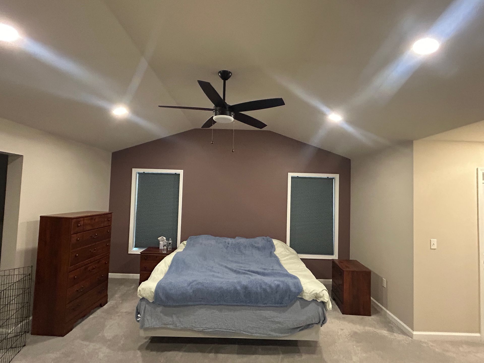 Bedroom with purple accent wall, bed, dresser, nightstands, and ceiling fan.