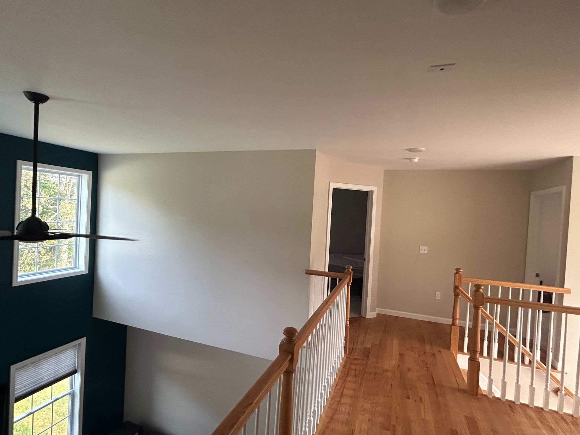 Interior view of a second-floor hallway with wooden floors, staircase, and a teal accent wall with a fan.