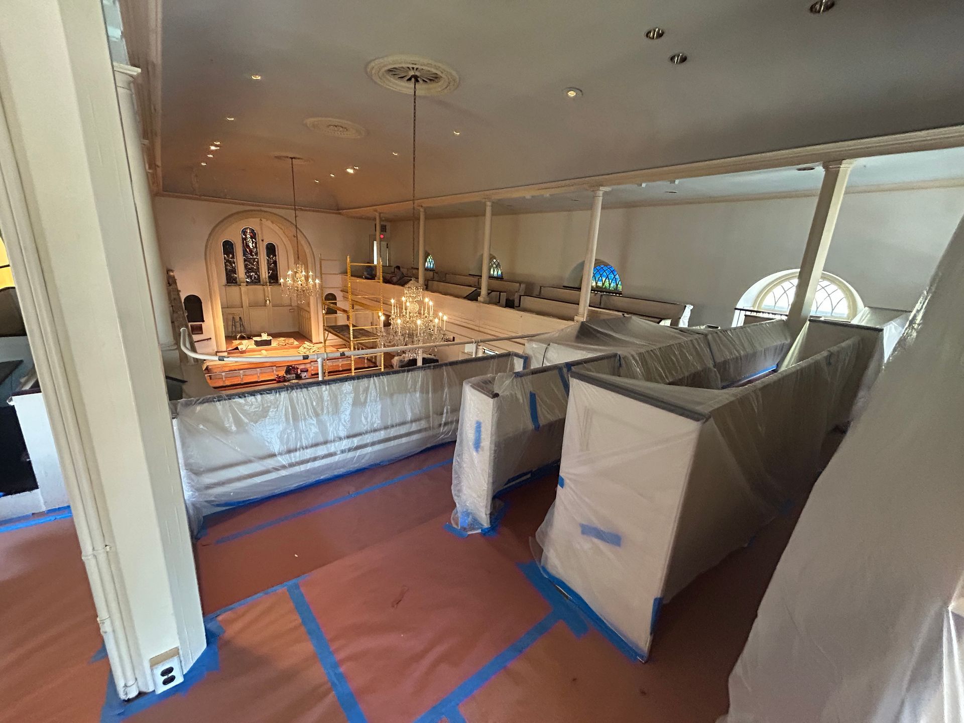 Interior of a building under renovation, with plastic covering furniture and orange floor protection.