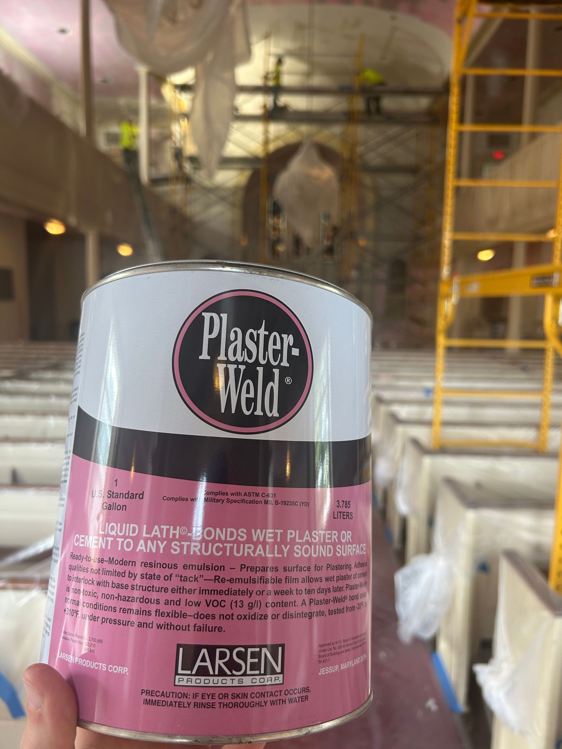 Can of Plaster-Weld held in front of a church interior under construction, scaffolding visible.