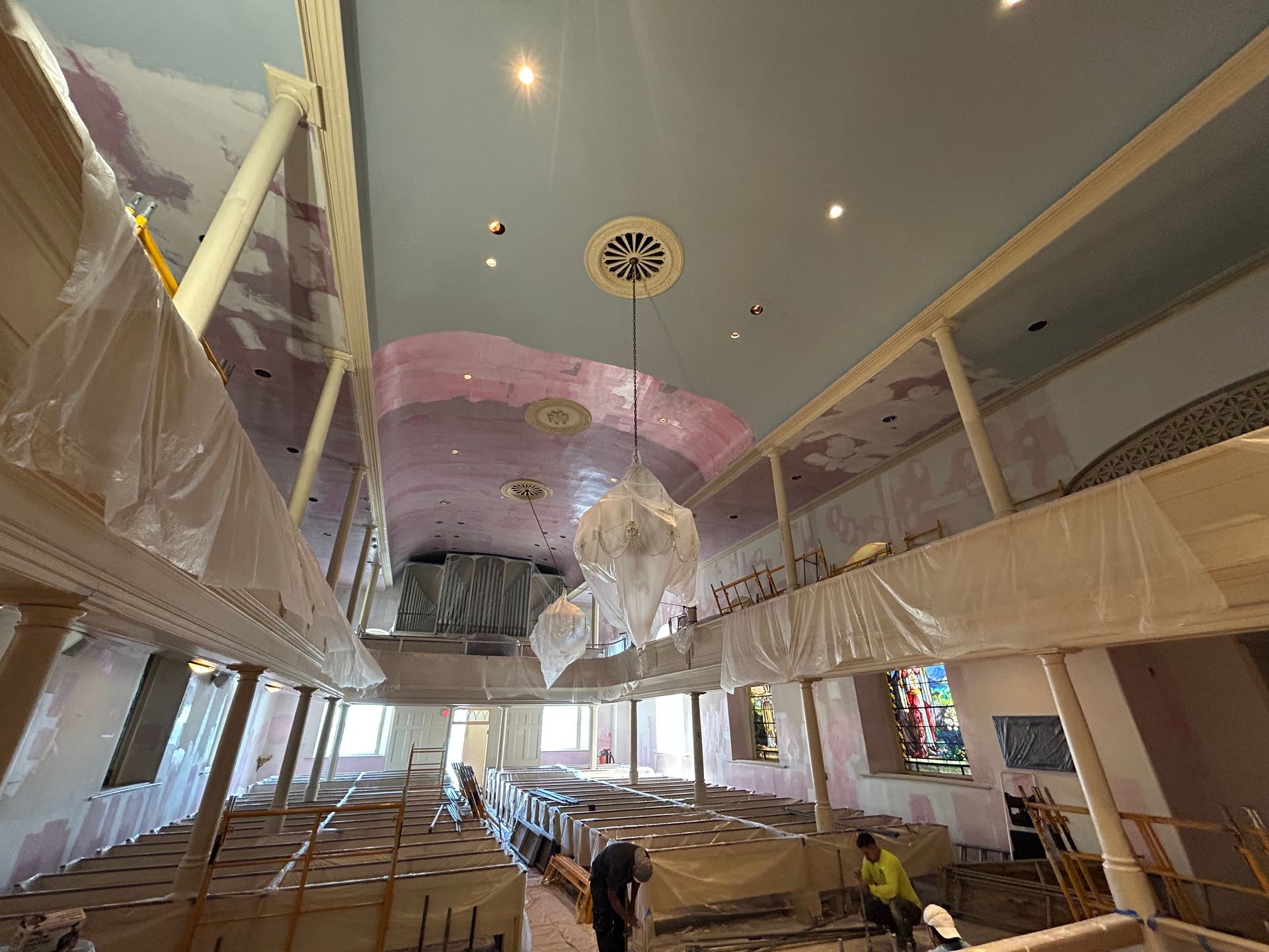 Interior view of a church under renovation; blue ceiling, scaffolding, plastic sheeting, and workers.