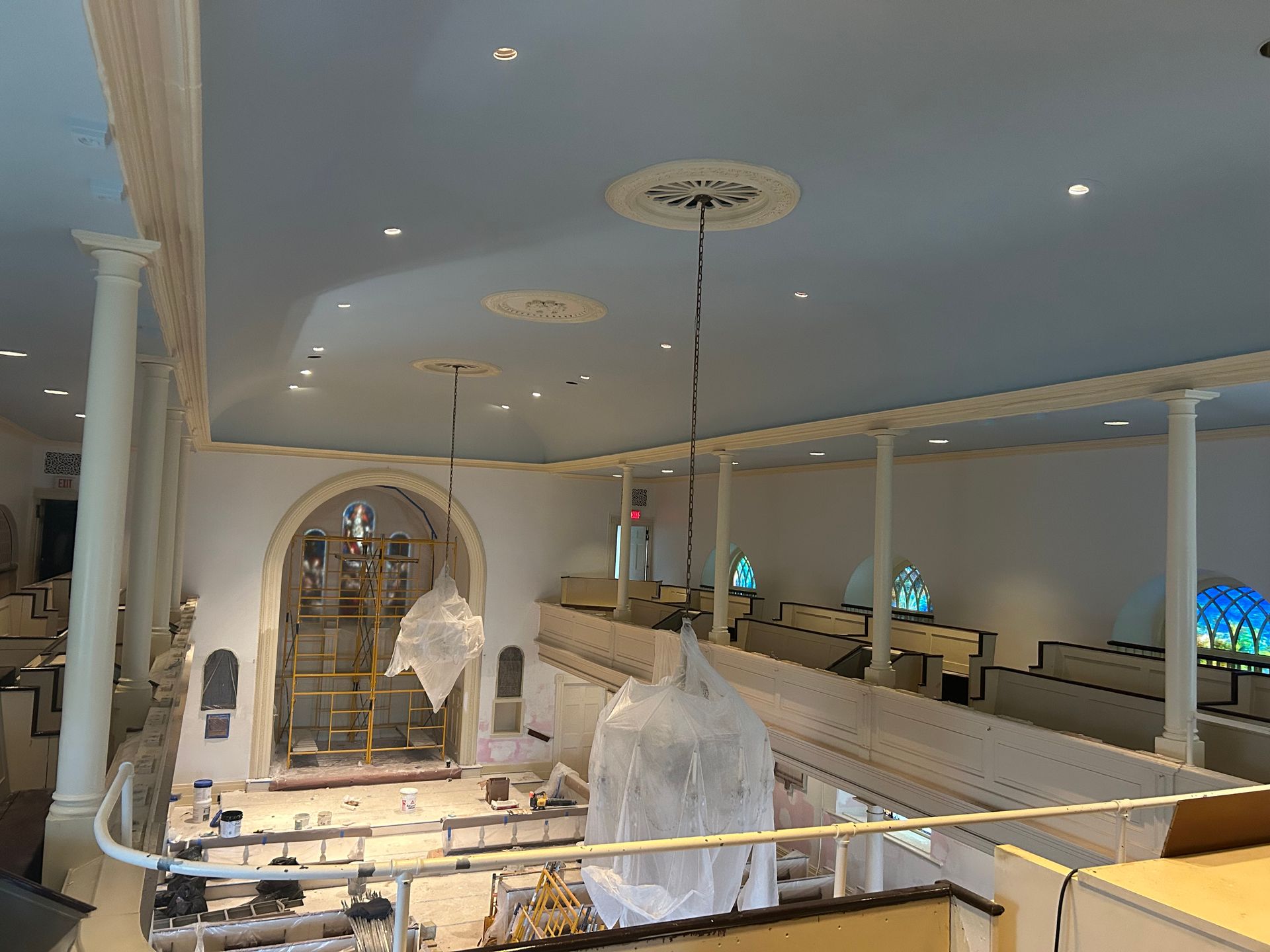 Interior view of a church under renovation, featuring a balcony, columns, and a light blue ceiling.