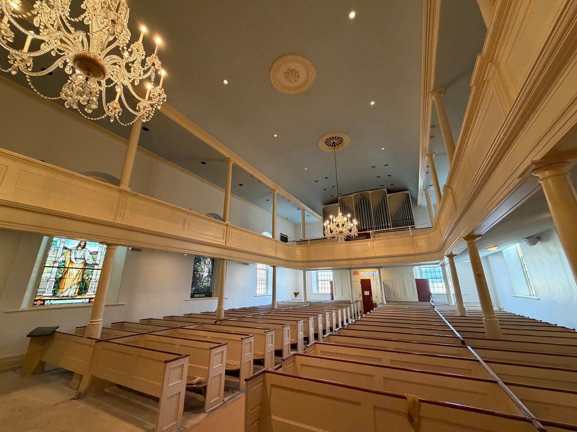 Interior of a church with rows of pews, balconies, stained glass windows, and a chandelier.