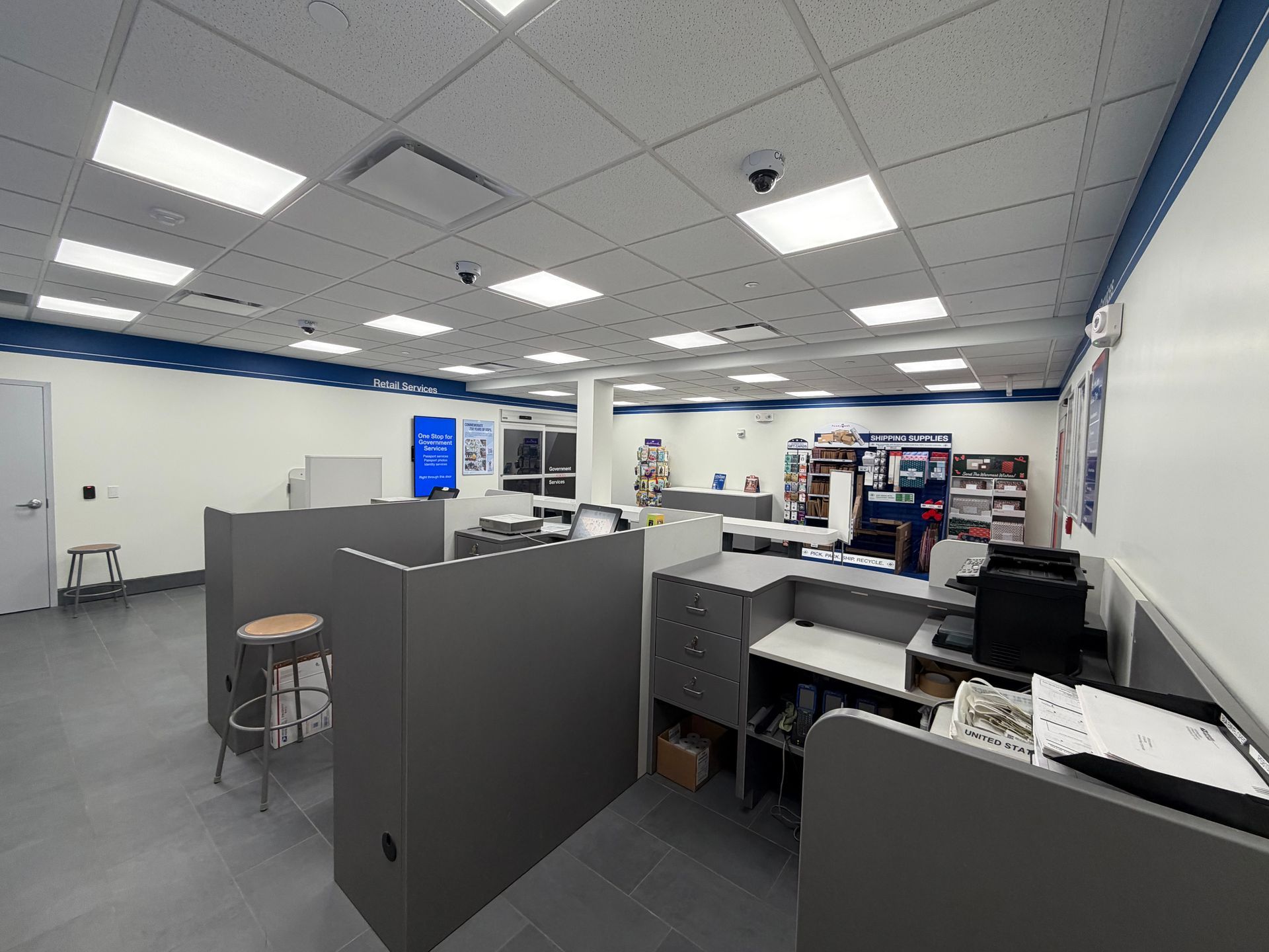 Interior of a post office with gray cubicles, bright ceiling lights, and postal service stations.