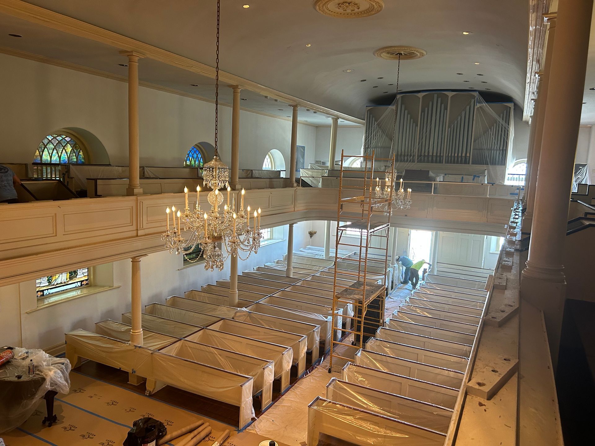 Interior view of a church under renovation. Pews are covered, balcony visible, and organ is shrouded.
