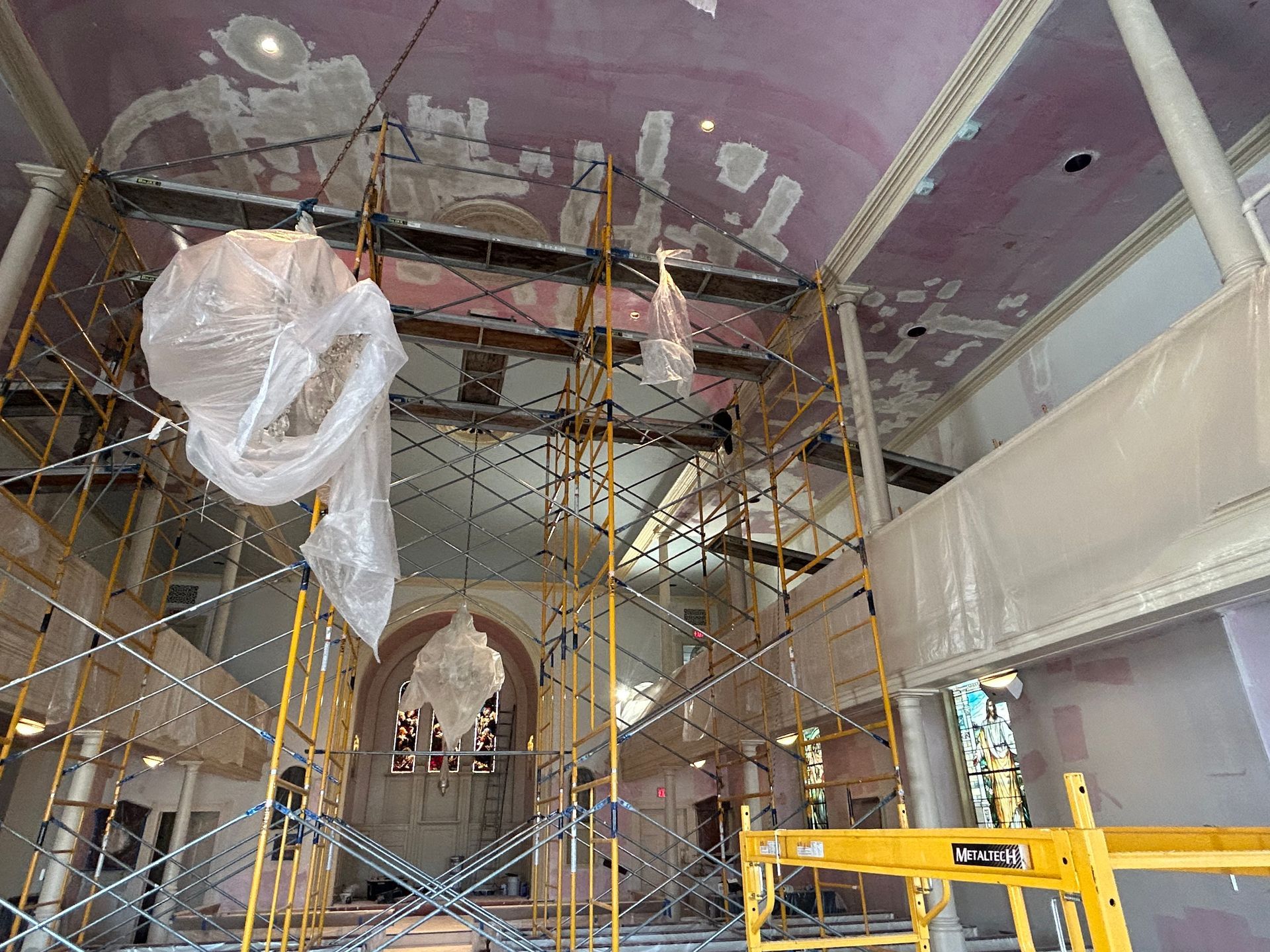 Interior of building under renovation with scaffolding, pink ceiling, and large light fixtures covered.