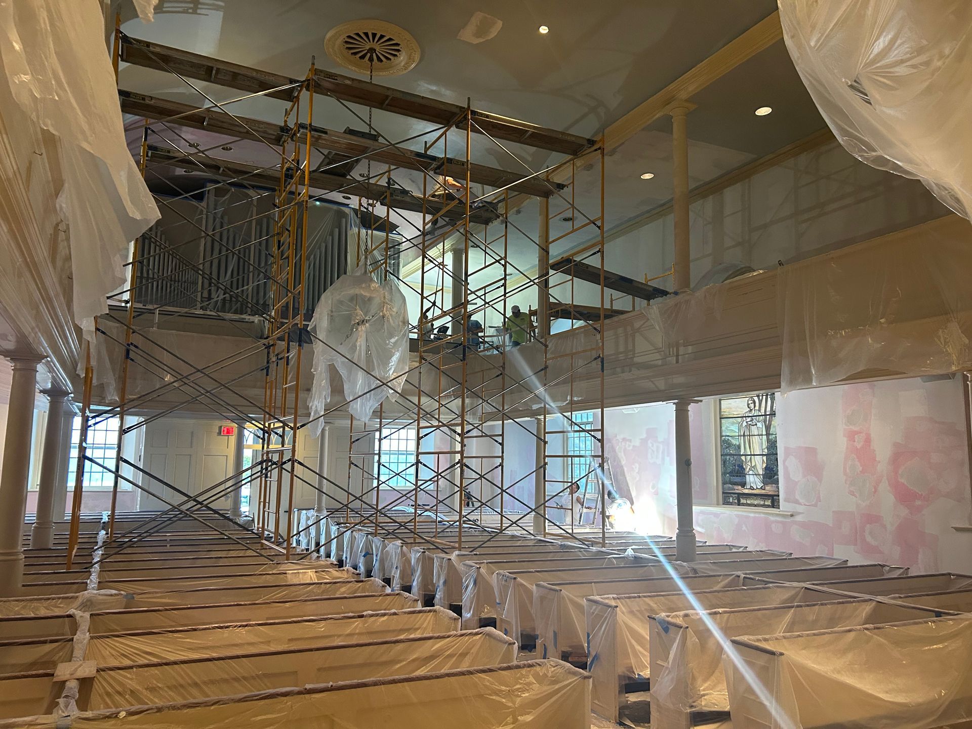 Interior view of a building under renovation with scaffolding, covered furniture, and plastic sheeting.