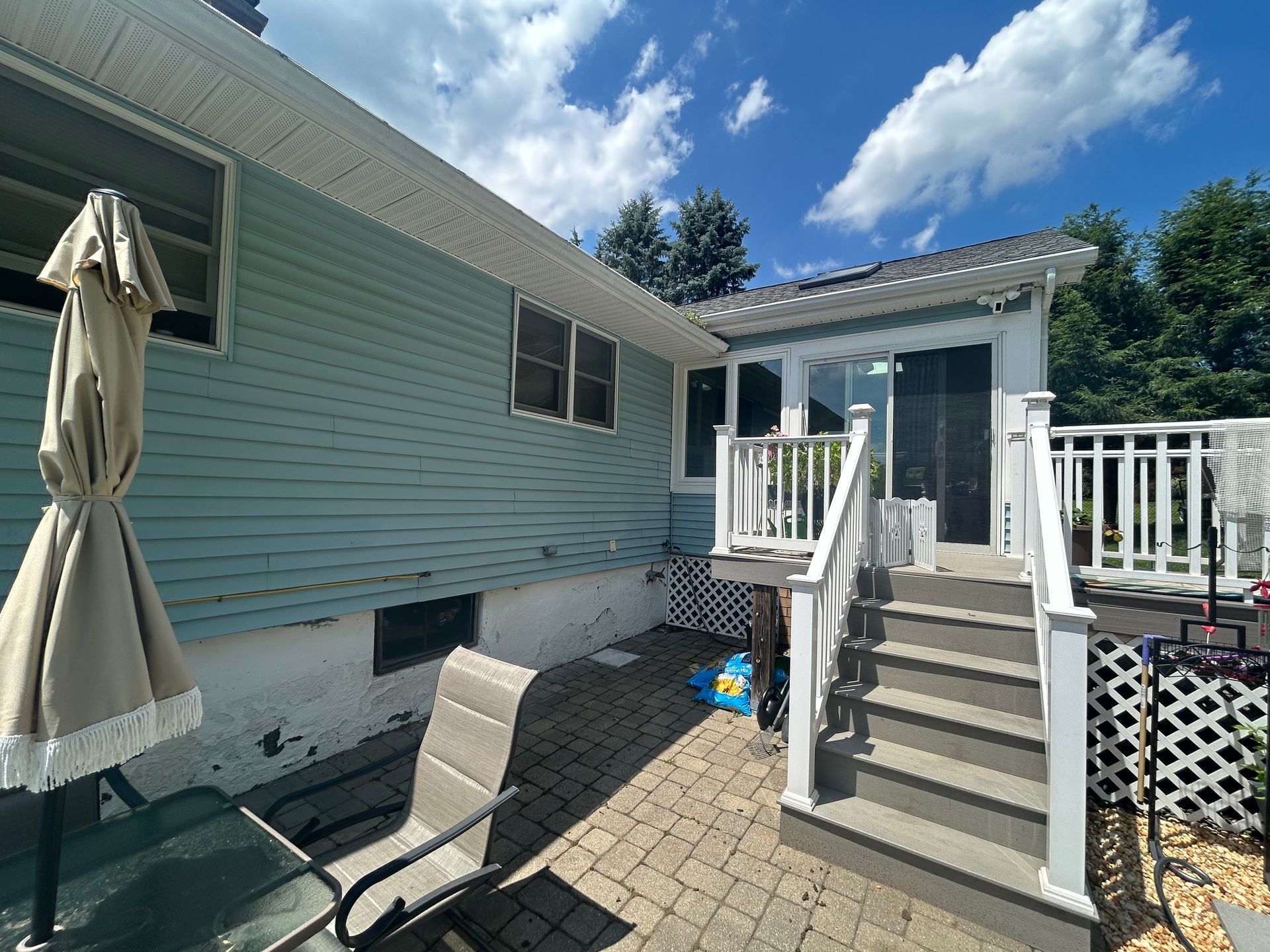 Backyard patio with deck and house. Turquoise siding, brick patio, white railing, blue sky.
