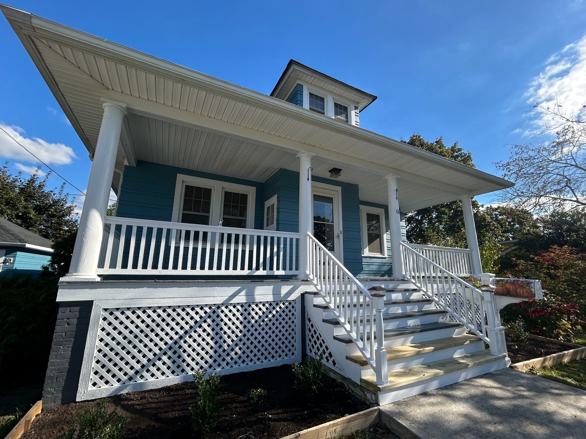 Blue house with white porch and steps under a blue sky.