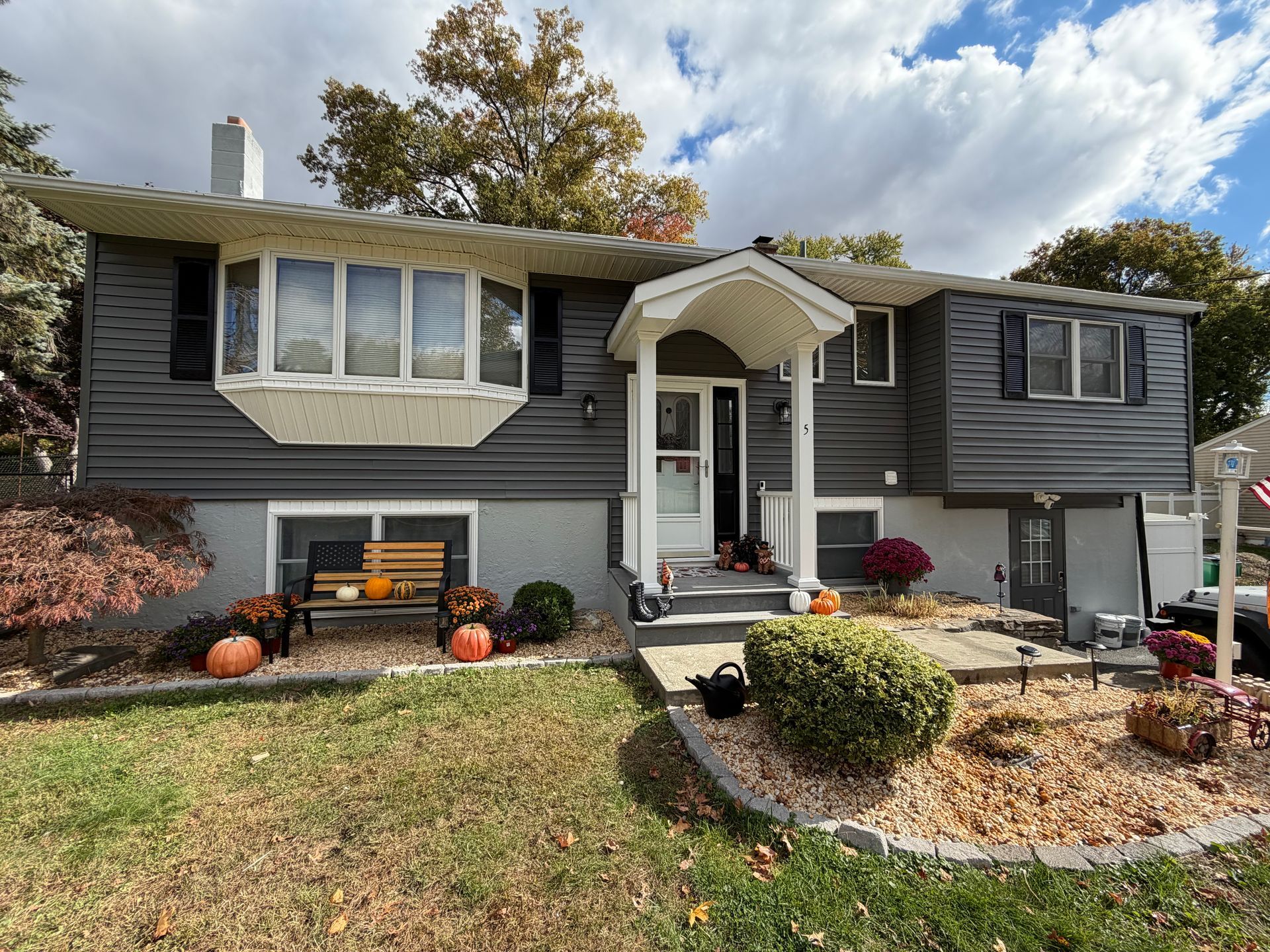 Gray house with white trim, bay window, and fall decorations in front yard.