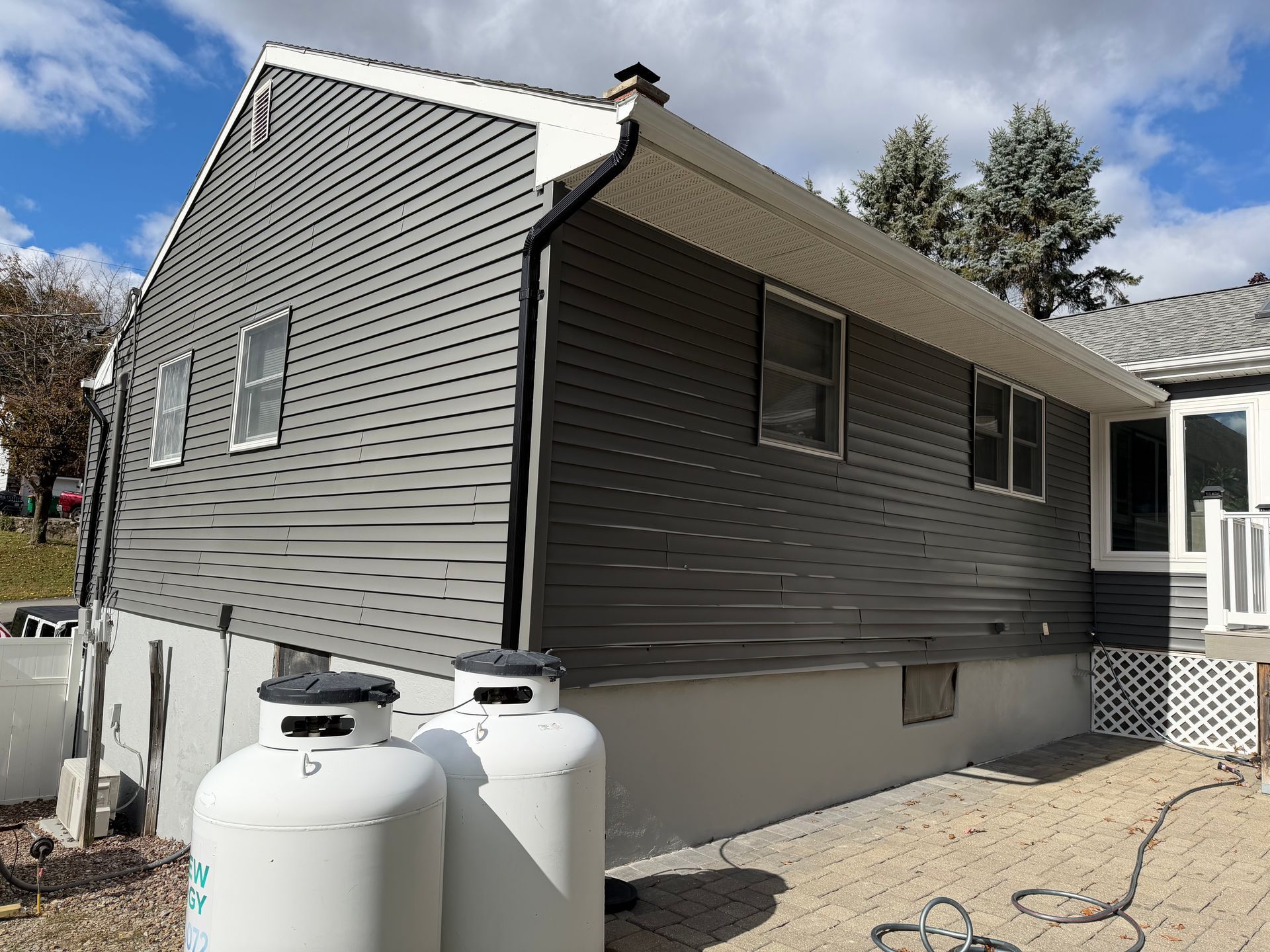 Gray siding on a house with white trim. Propane tanks sit below. Blue sky.
