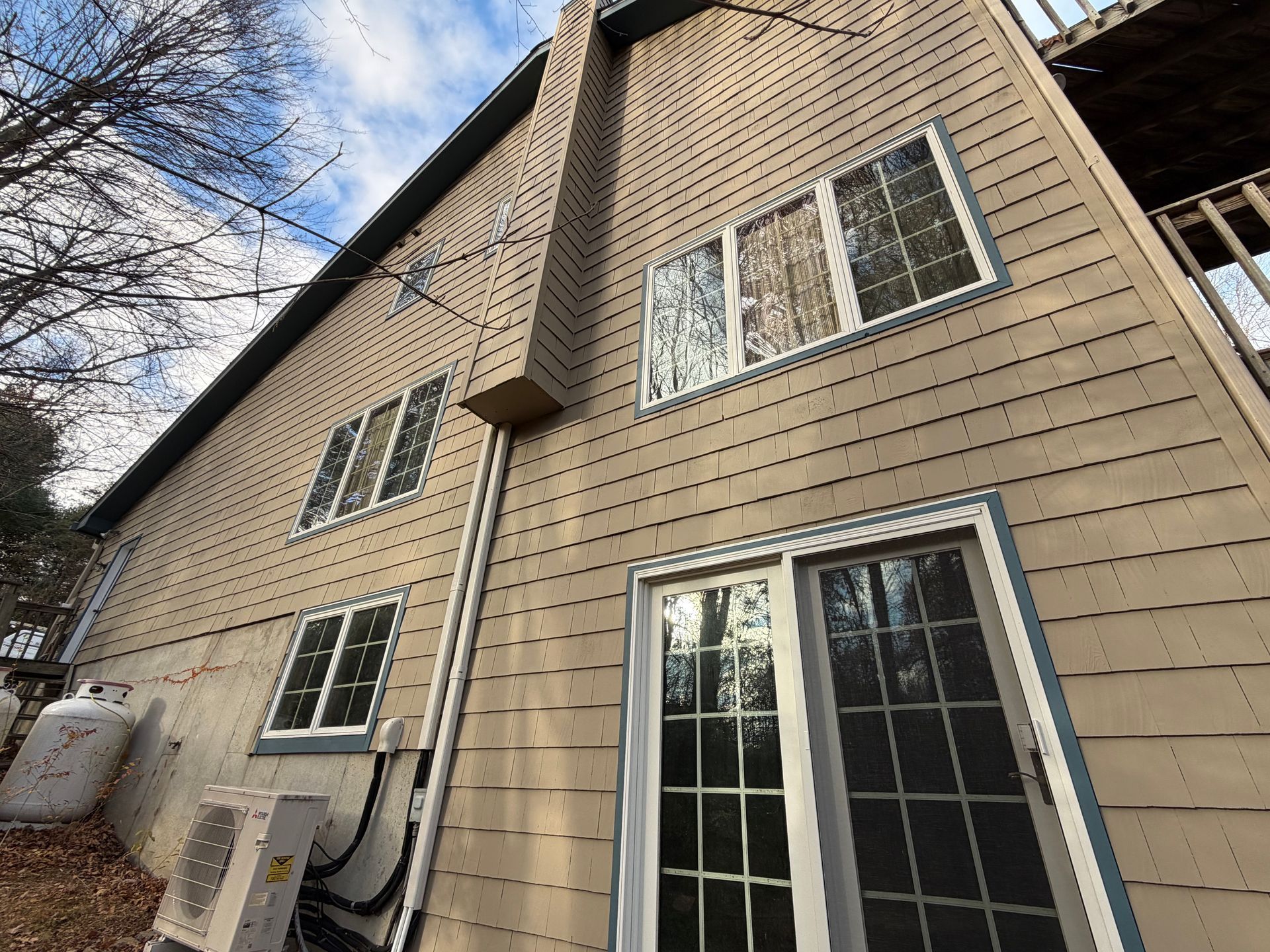 Tan siding on a two-story building with multiple windows and a sliding glass door. A chimney is visible.
