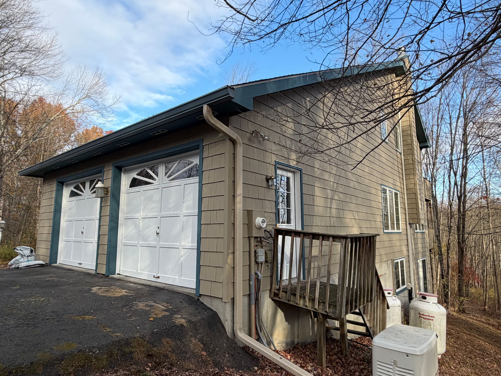 Tan-sided house with two garage doors. Blue trim, white doors, and a deck are visible.
