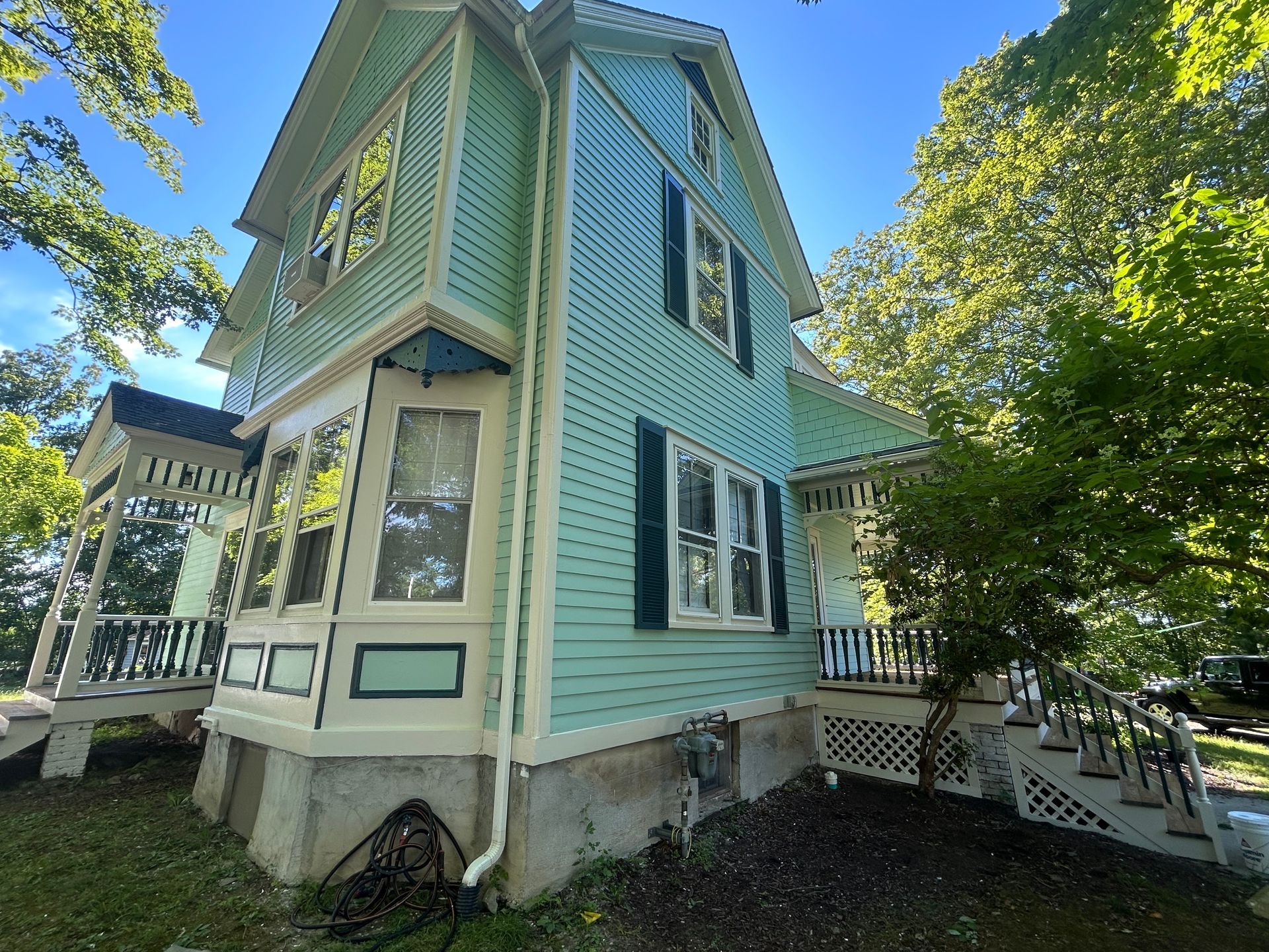Light green Victorian house with black shutters, beige trim, and a porch.
