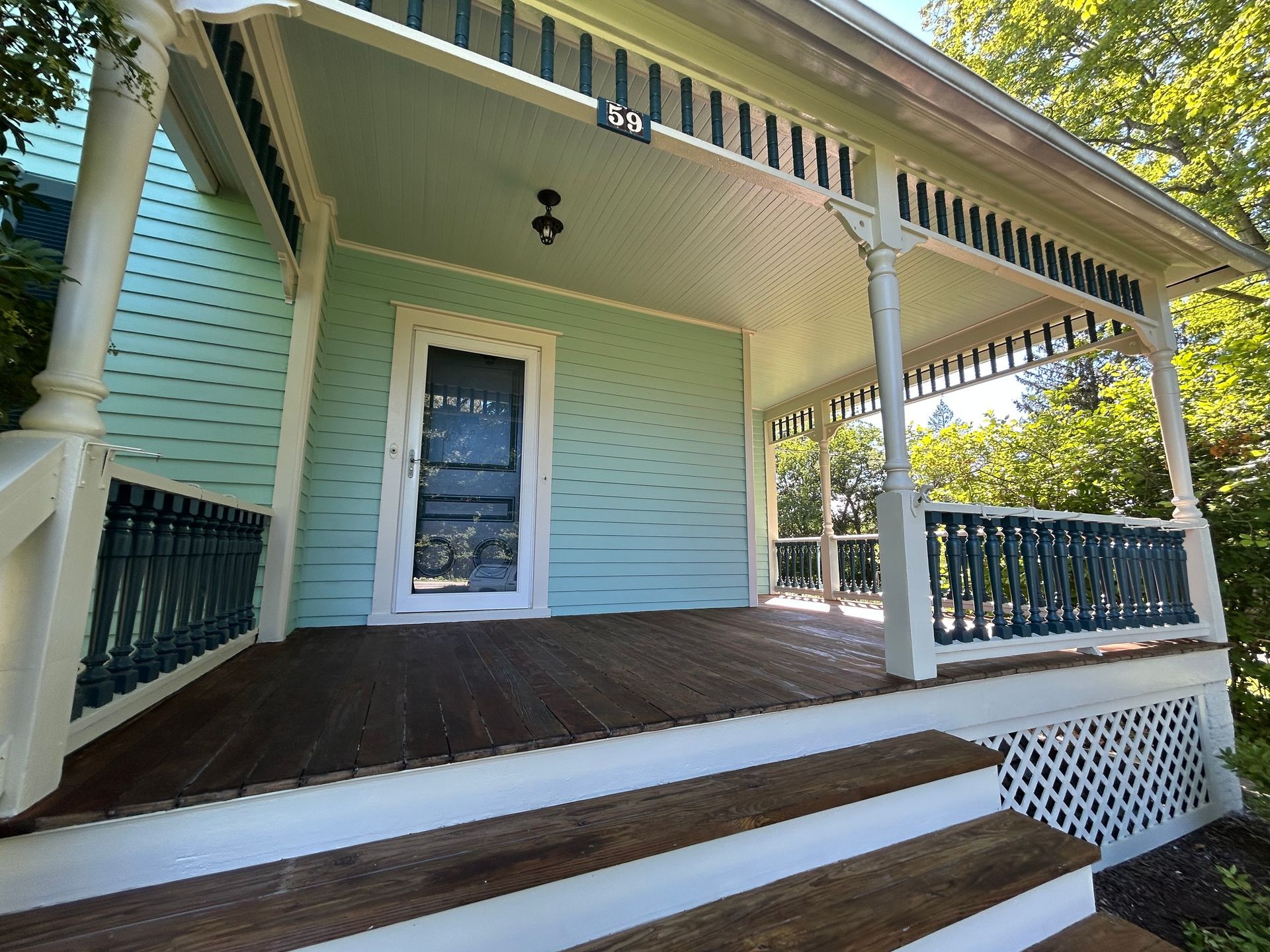 A light blue house with a covered porch. Wooden steps lead to the porch with dark wood decking and white trim.