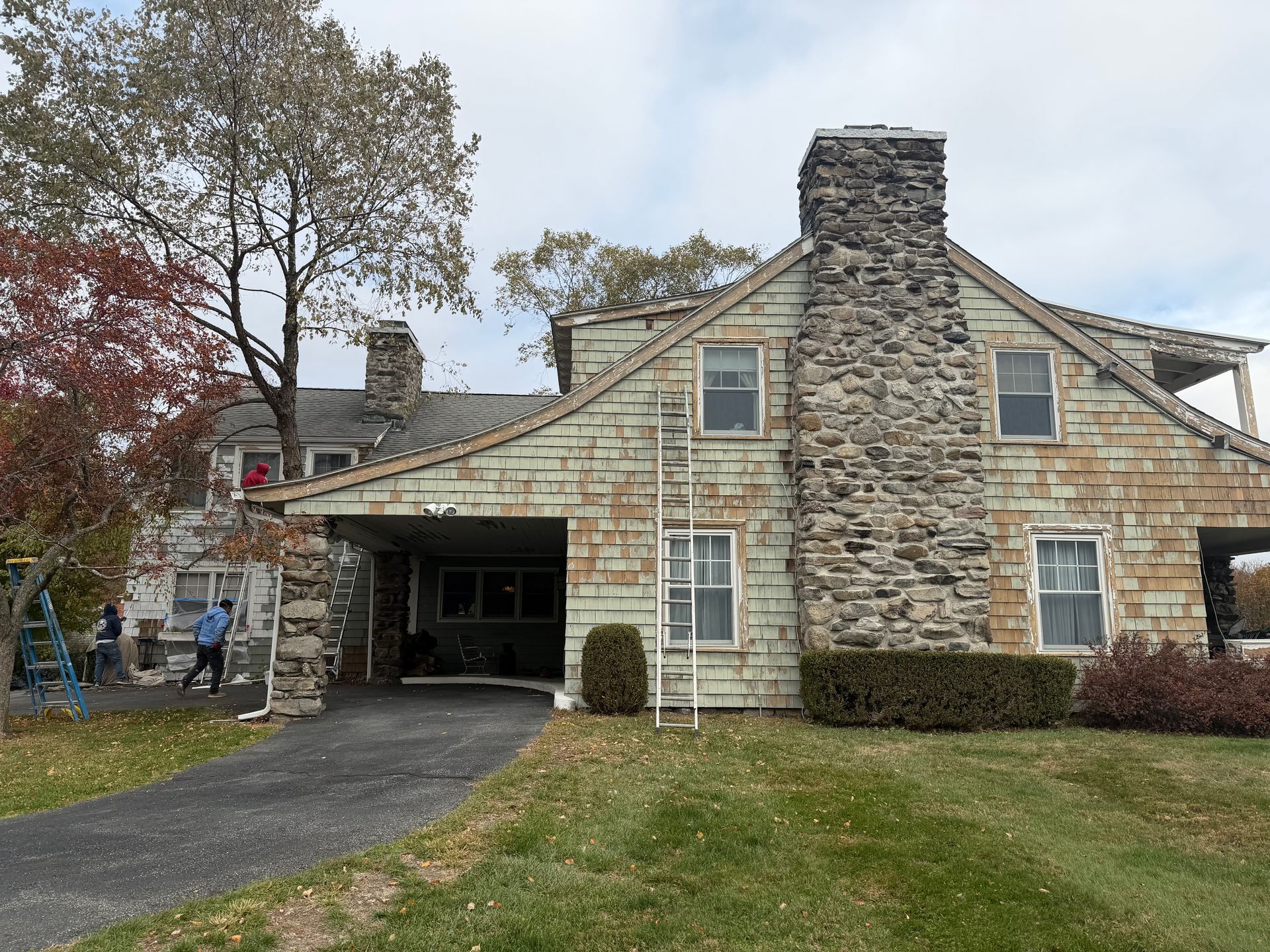 Stone house with peeling green paint, two chimneys, and driveway.