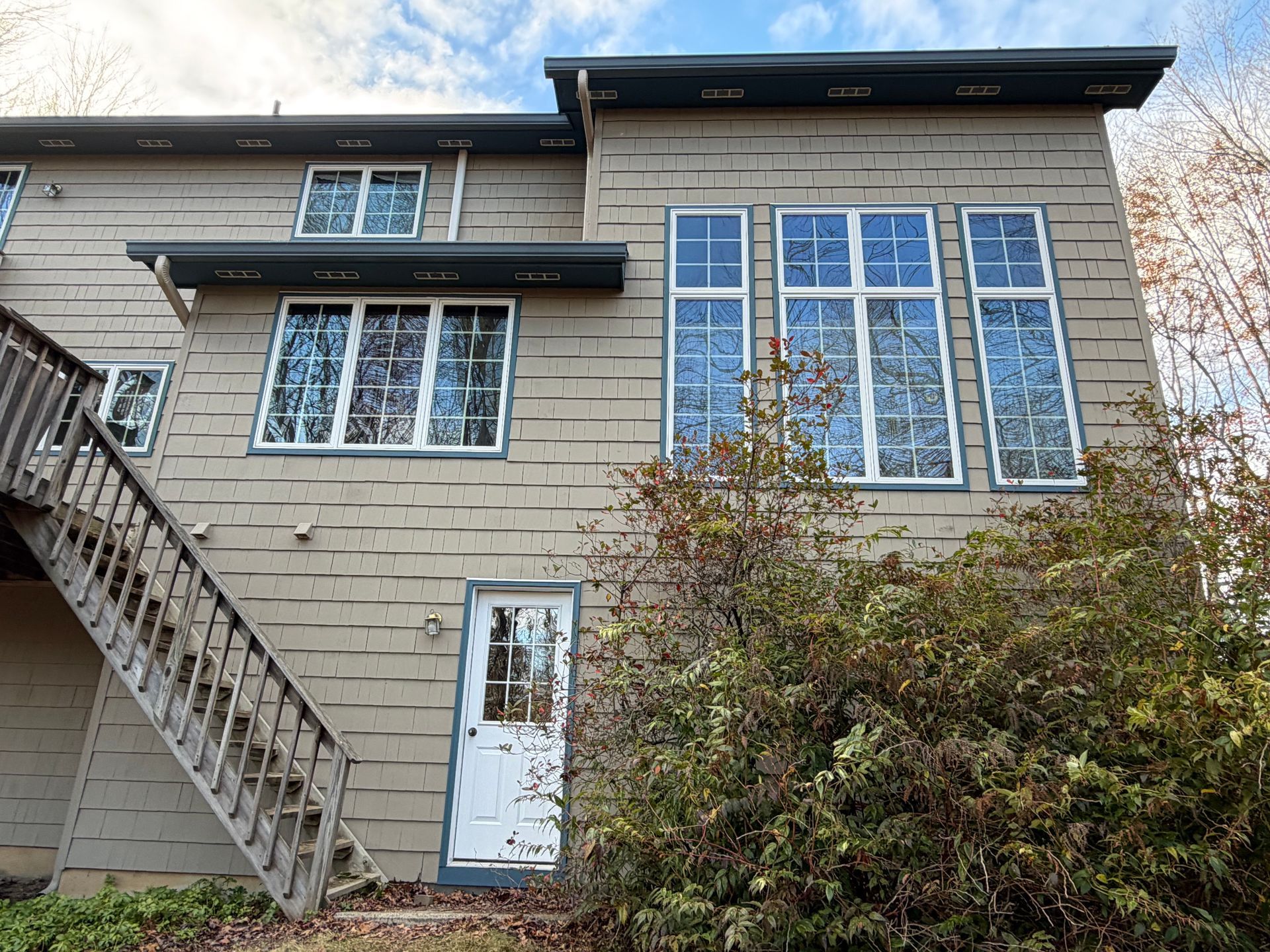 Exterior of a two-story building with multiple windows and a staircase, weathered beige siding, and white door.