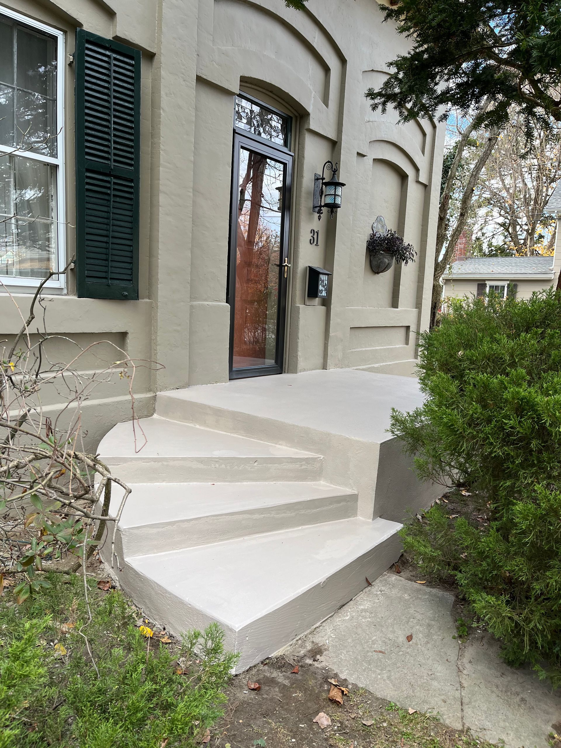 Concrete steps leading up to the front door of a light-colored building with dark shutters.