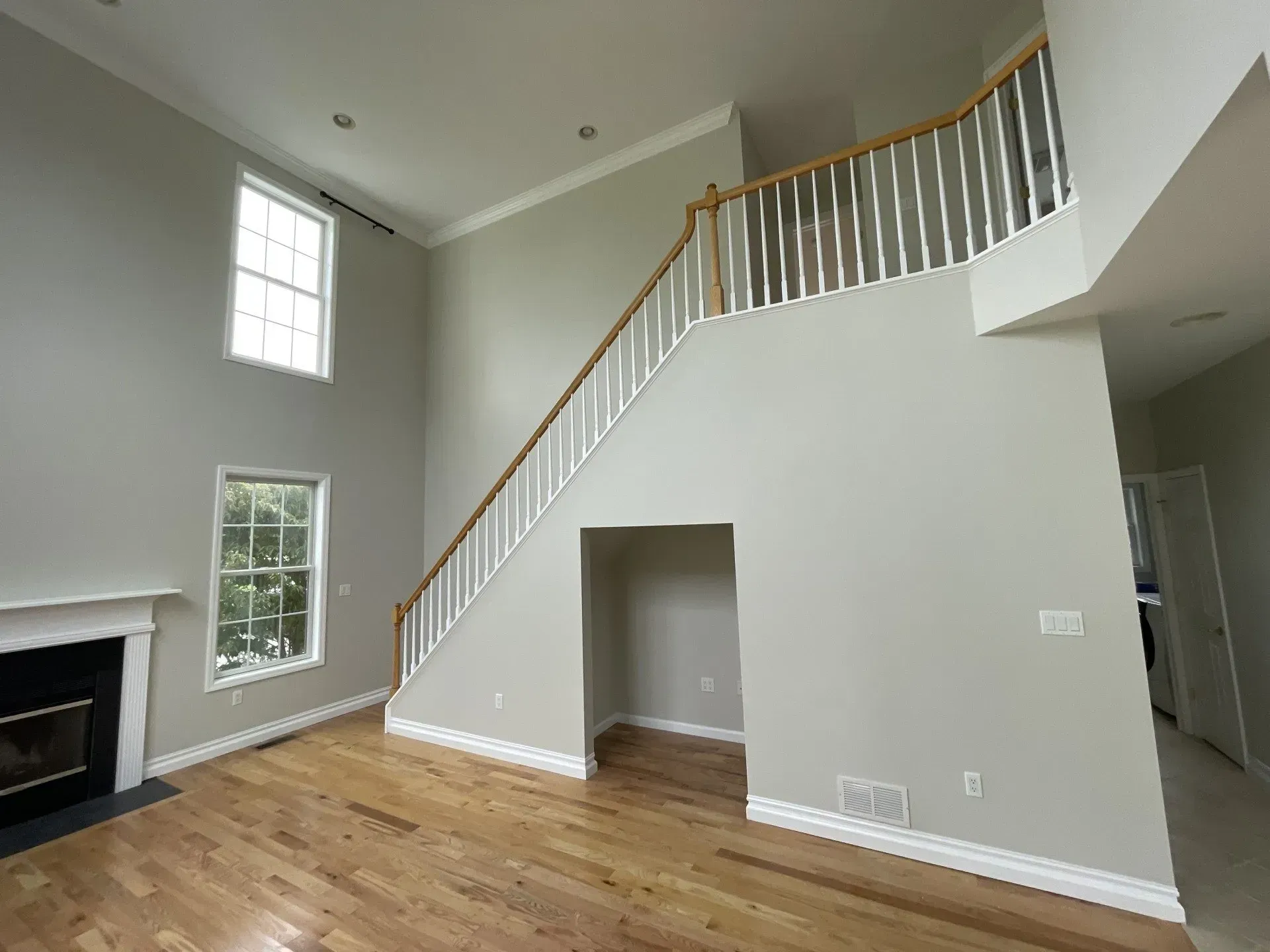 Interior view of a living room with hardwood floors, a staircase, and fireplace. Walls are painted gray.