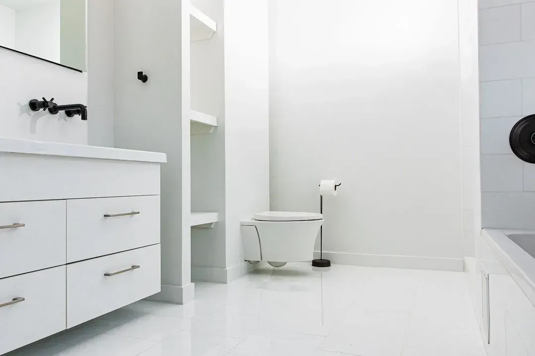 White bathroom with vanity, toilet, and shelves; black faucet and fixtures.