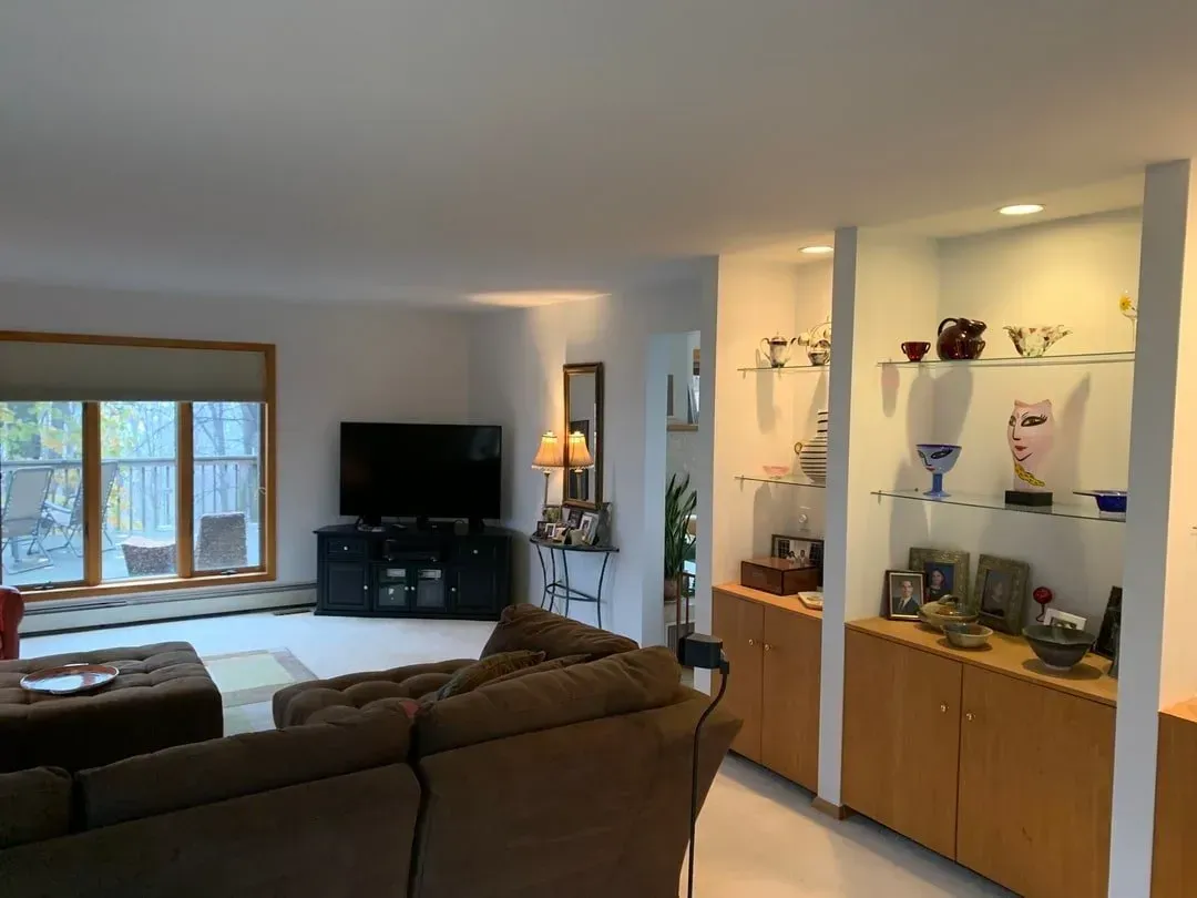 Living room with TV, brown couch, built-in display shelves with objects, and a window.