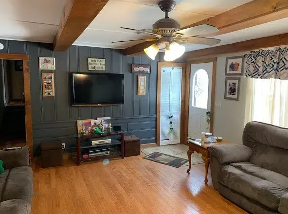 Living room with wood-paneled walls, TV, ceiling fan, sofa, and wooden beams.