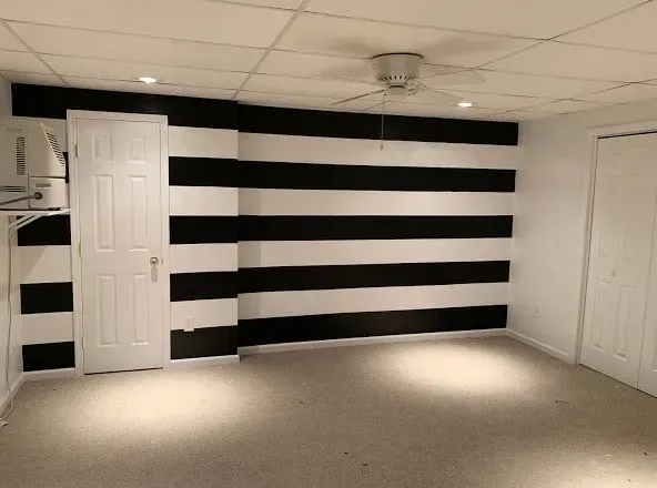 Room with black and white horizontal stripes on one wall, white doors, tan carpet, and a ceiling fan.