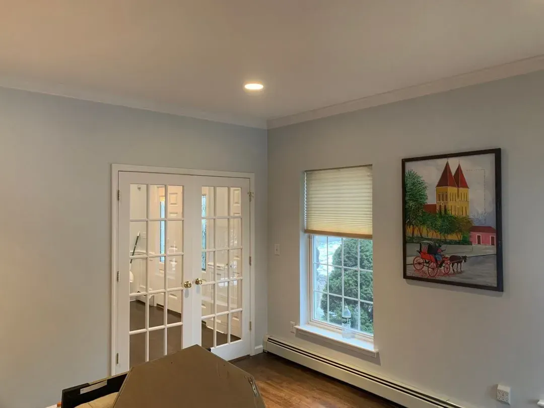 Interior room with French doors, a window with blinds, and a painting on the wall. Pale blue walls and white trim.