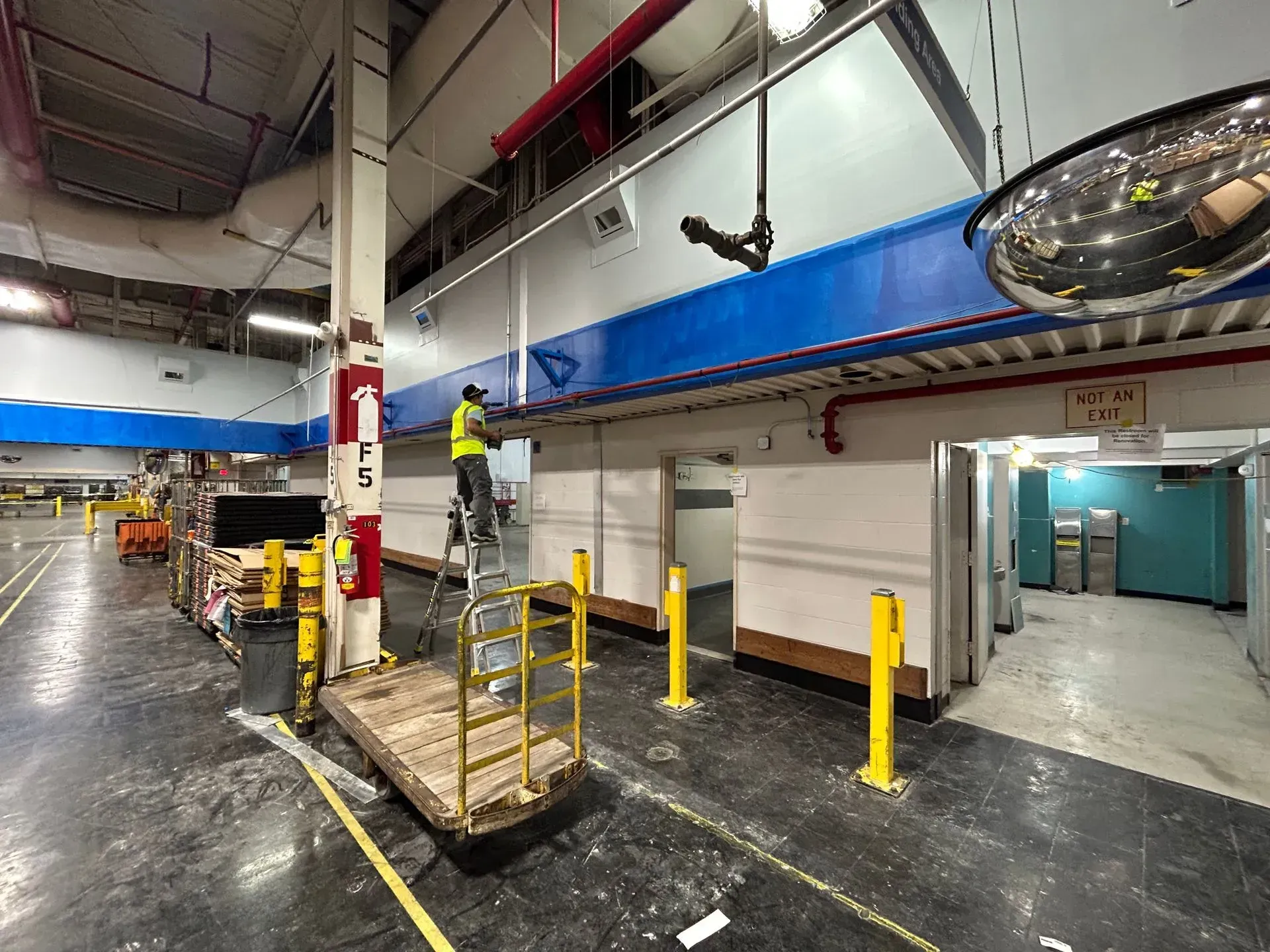 Warehouse interior with worker on a ladder, near loading equipment and a row of doors.