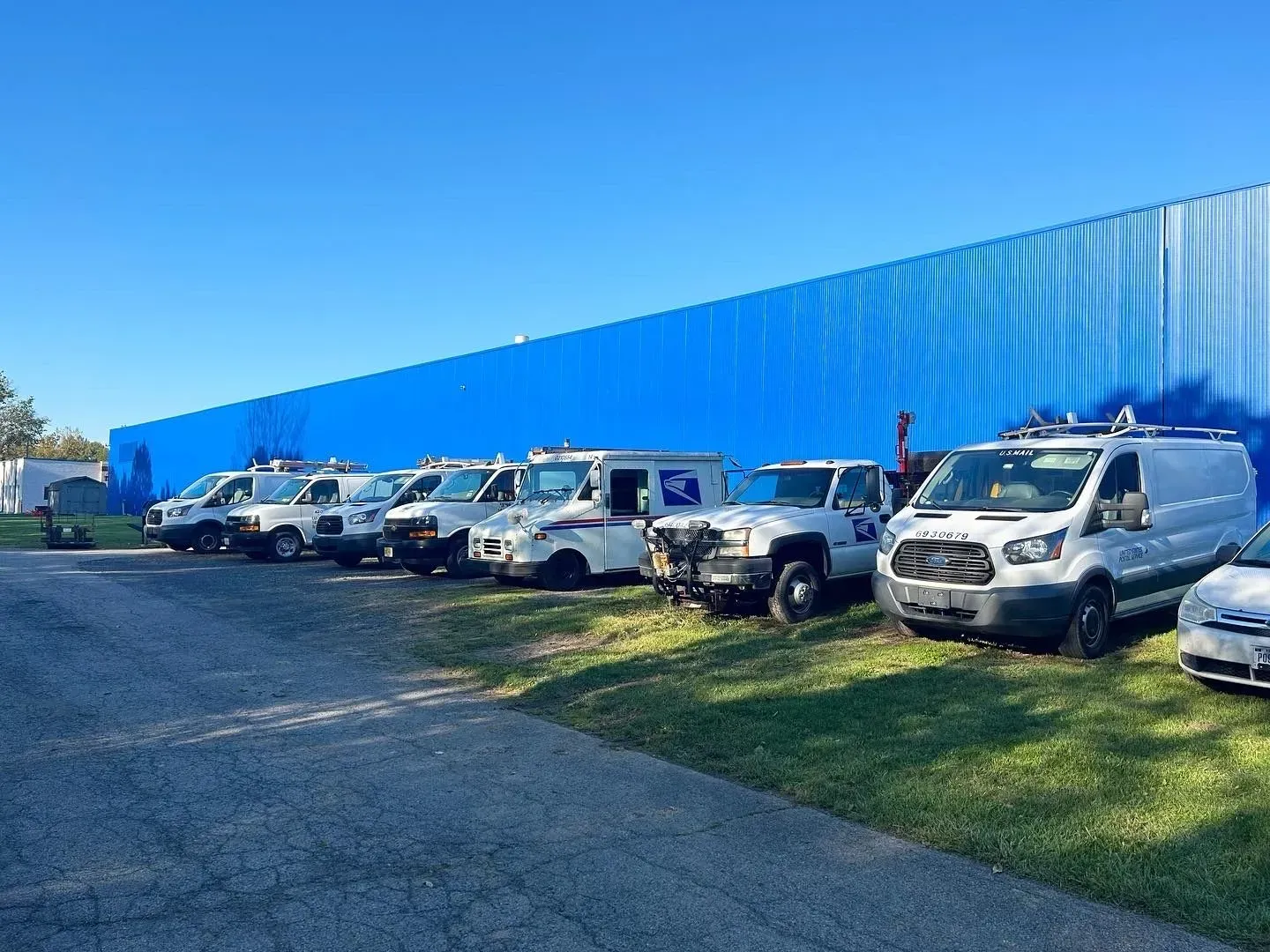 Several white service vehicles parked in a row in front of a blue wall. Bright sunny day.