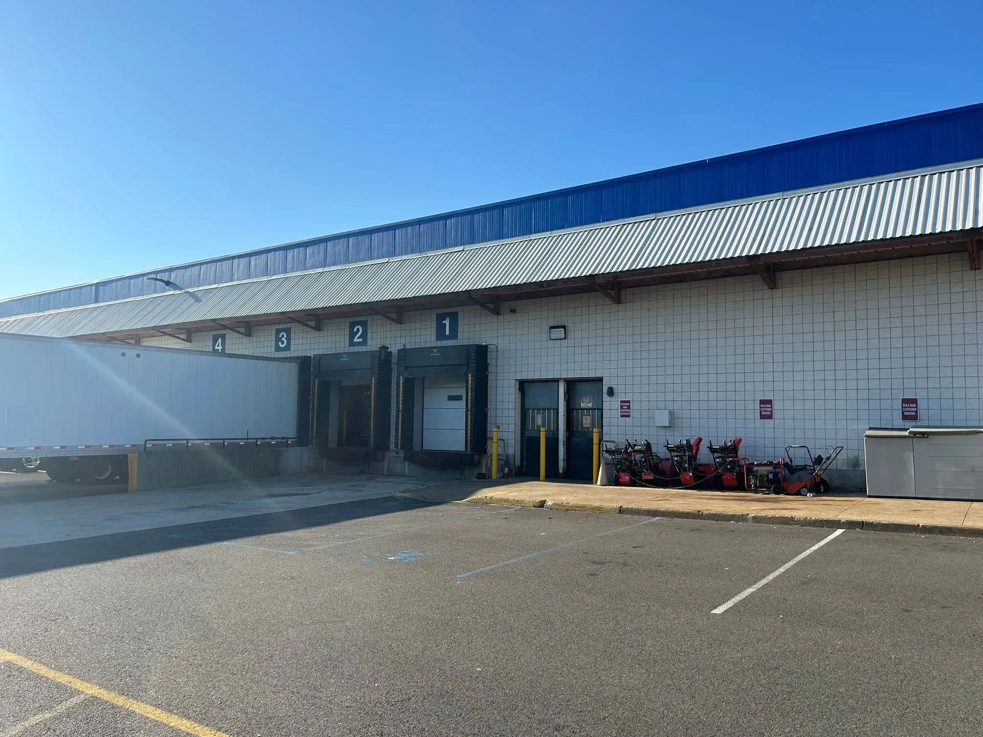 Loading docks of a warehouse. A semi-trailer is backed into one dock. Snowblowers sit nearby.
