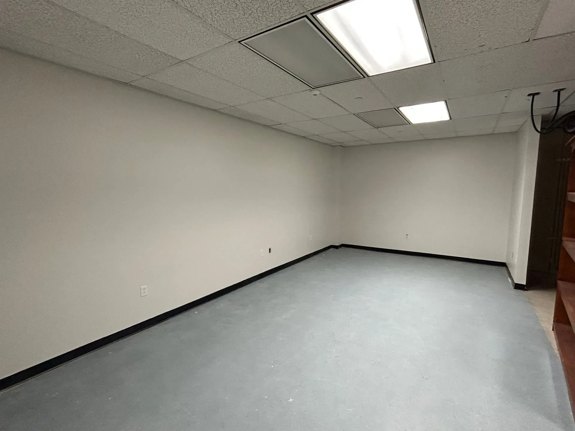 Empty office room with gray floor, white walls and ceiling, overhead lights.