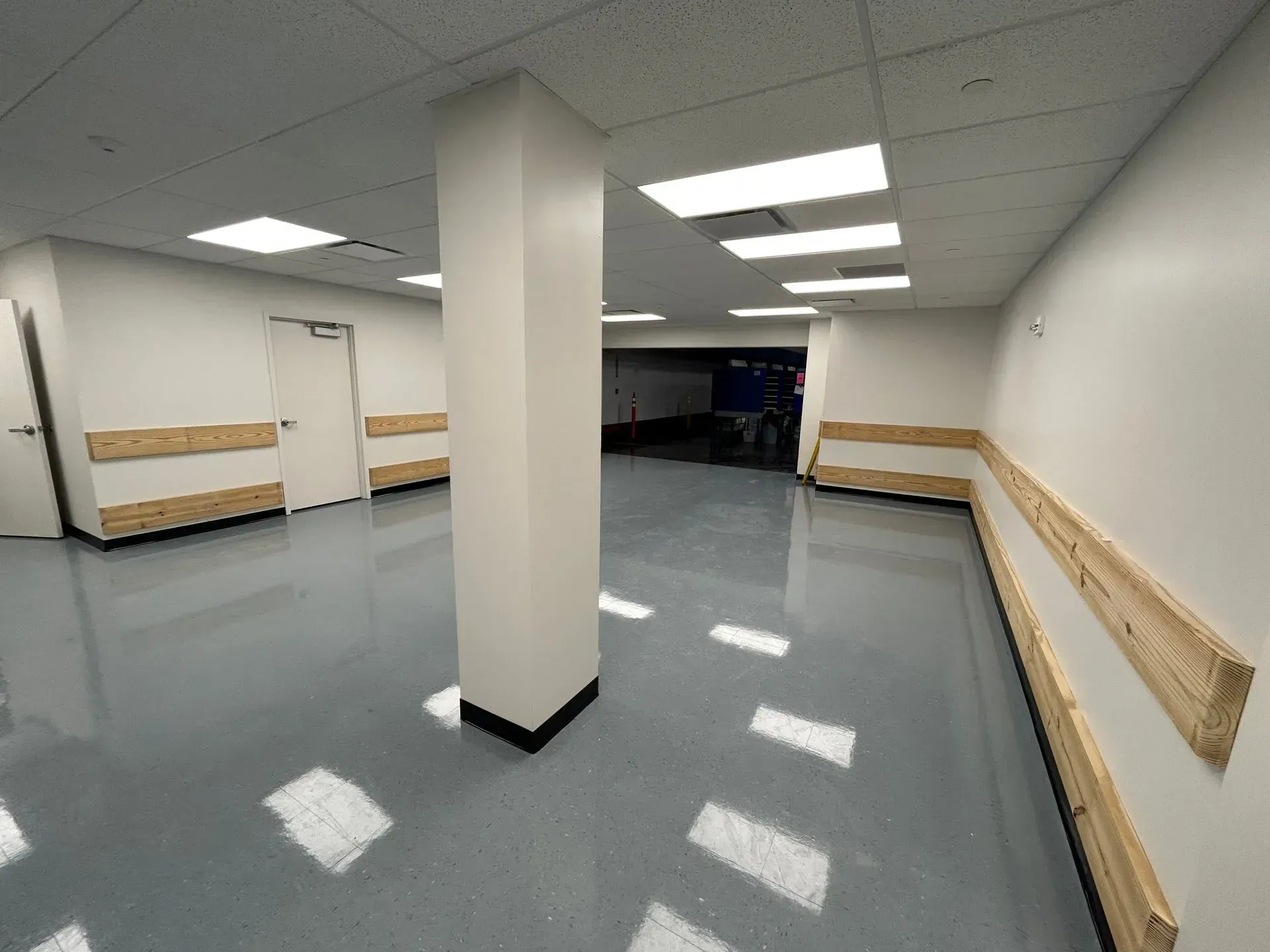 Empty, long hallway with white walls, a gray floor, and a central white pillar.