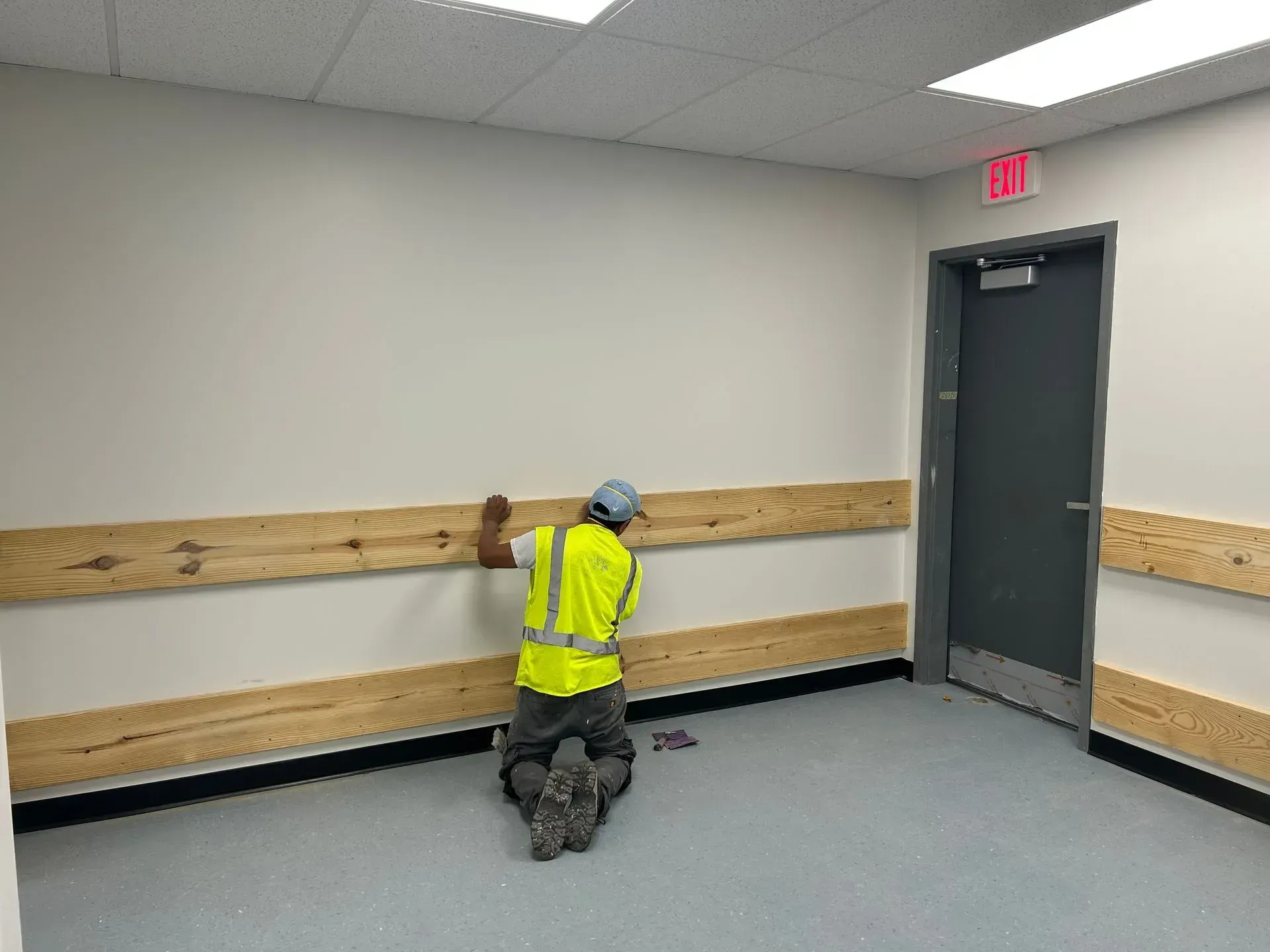Person installing wood paneling on wall in a room, wearing a safety vest.