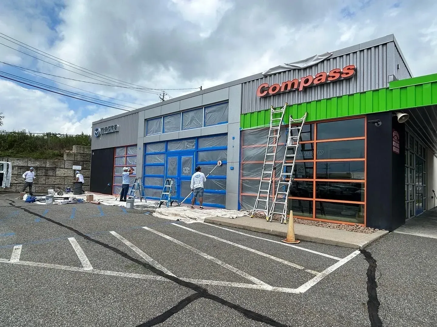 Exterior of a building under renovation, with workers painting. Compass sign on the roof.