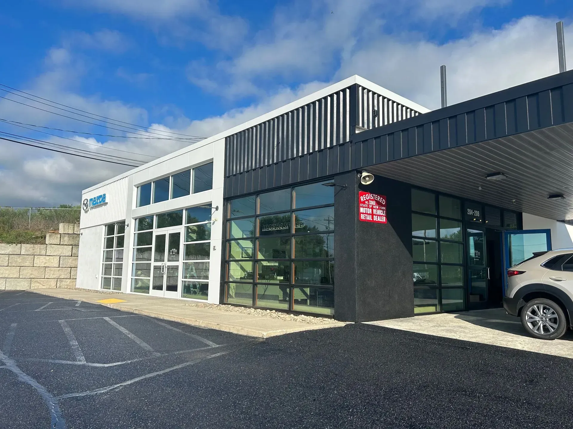 Modern commercial building with glass windows, black accents, and a vehicle parked on the right.