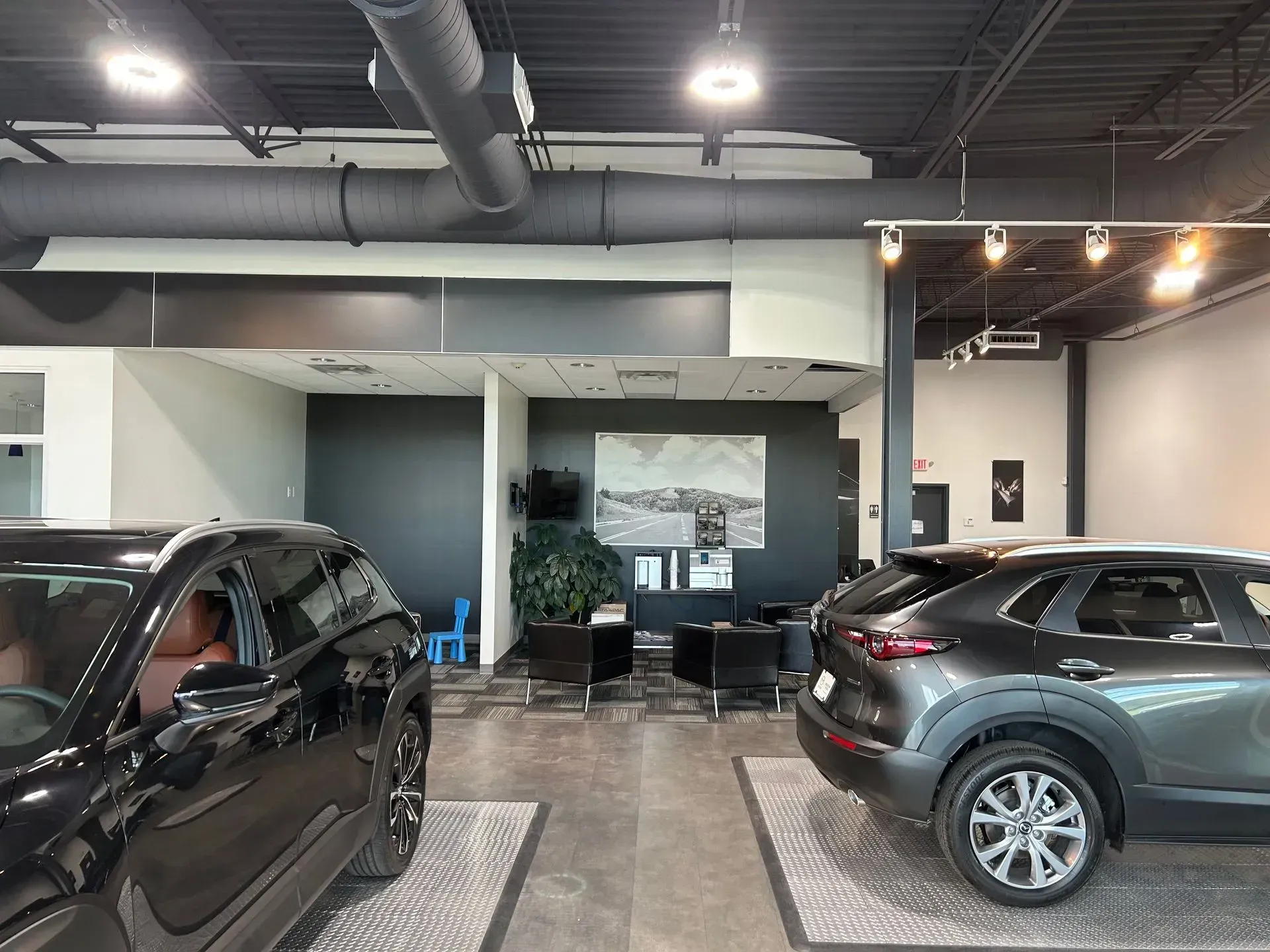 A car showroom interior with two SUVs, seating area with artwork, and a dark ceiling.