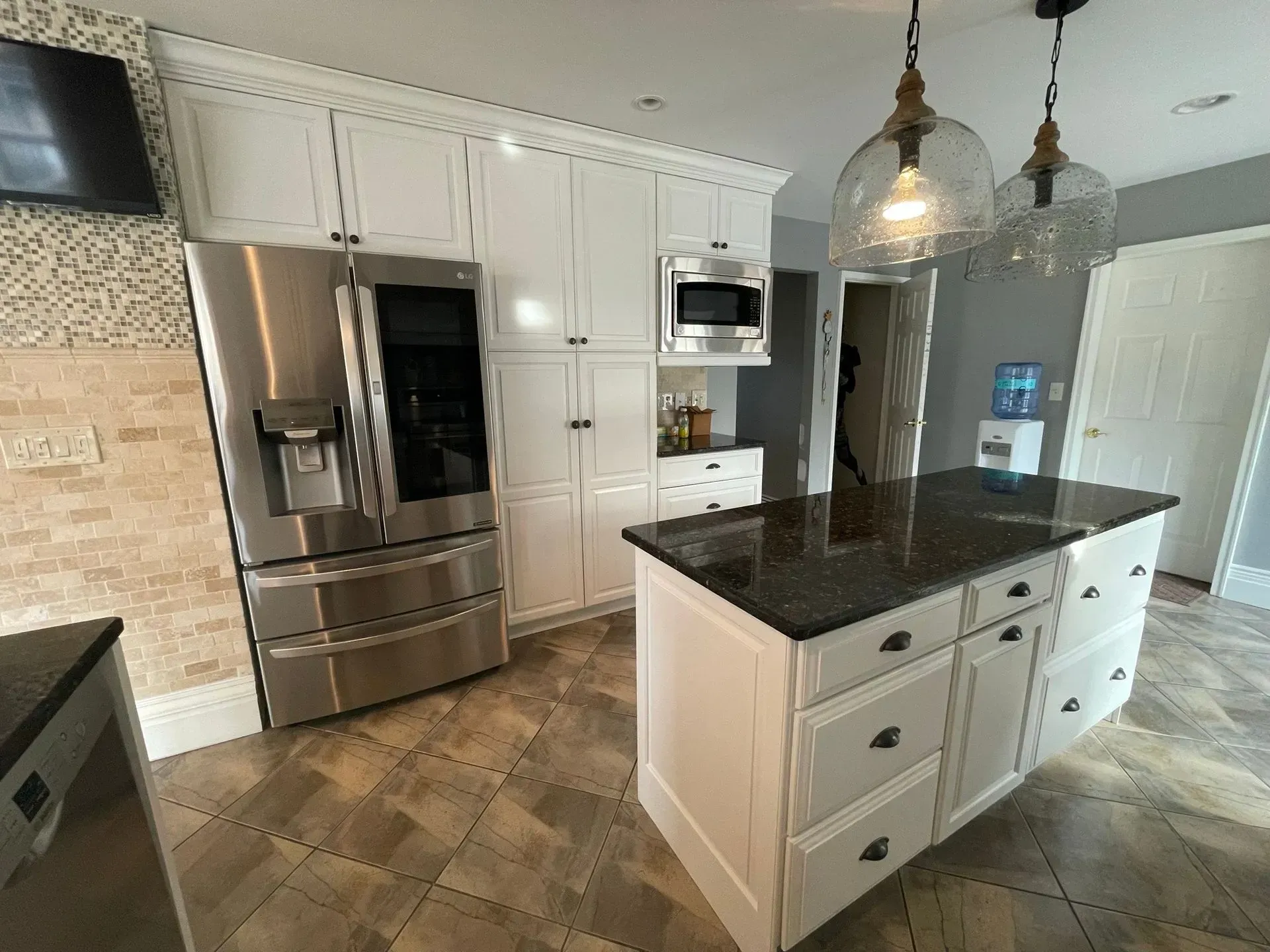 White kitchen with stainless steel appliances, dark countertops, and an island with overhead lighting.