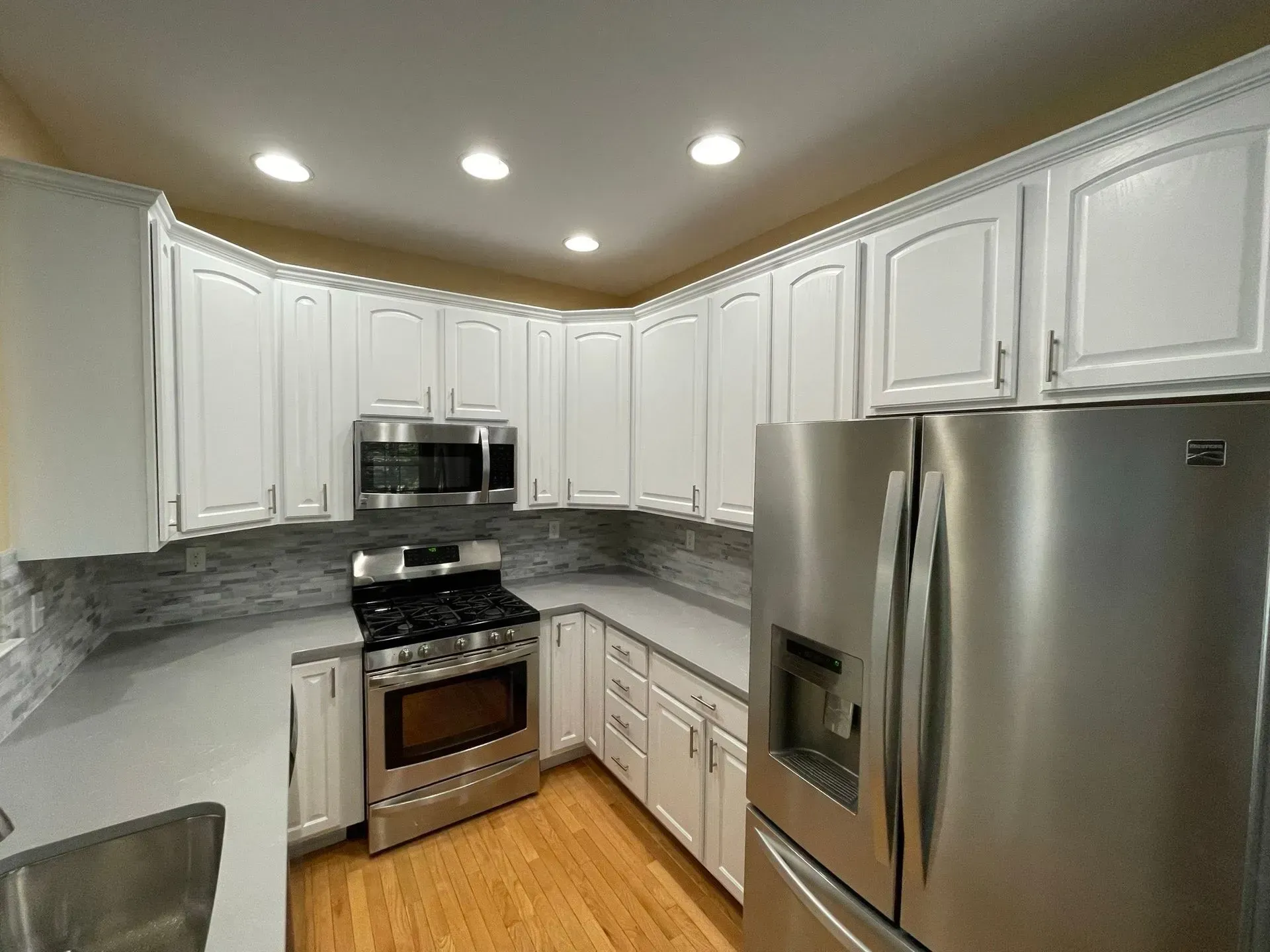 White kitchen with stainless steel appliances and light-colored countertops.