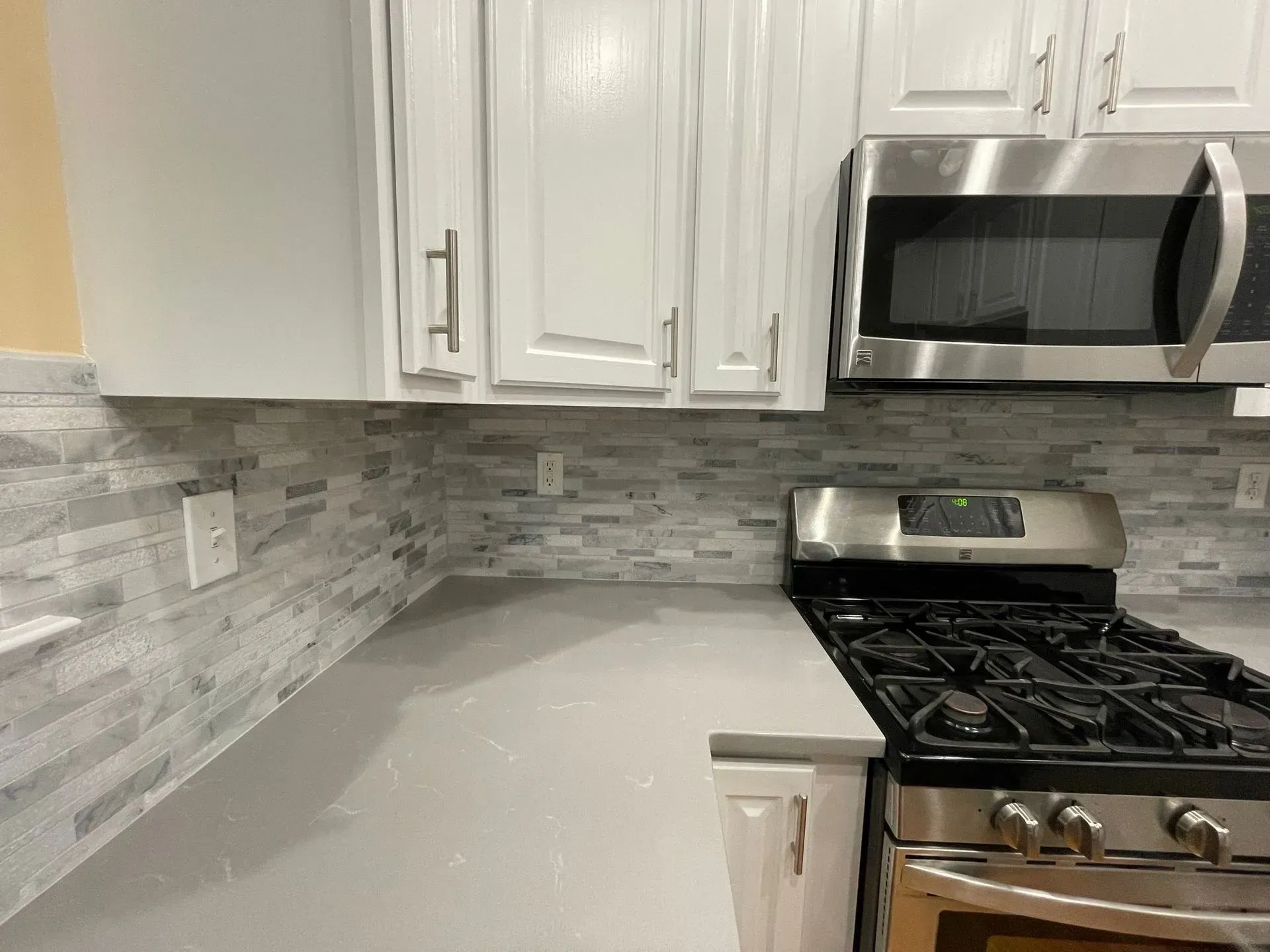 Kitchen counter with white cabinets, stainless steel appliances, and grey tile backsplash.