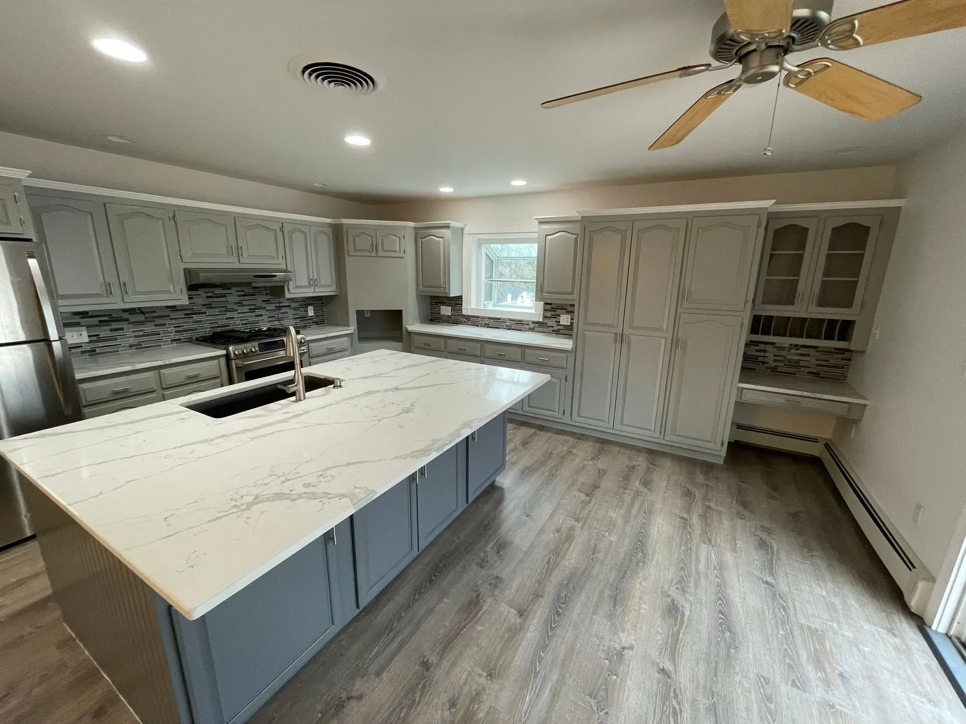 Spacious kitchen with gray cabinets, large island with white countertop, and light wood-look flooring.